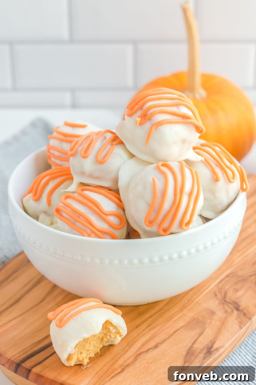 A White Chocolate Pumpkin Truffle on a bowl with one outside, bitten, tempting the viewer.