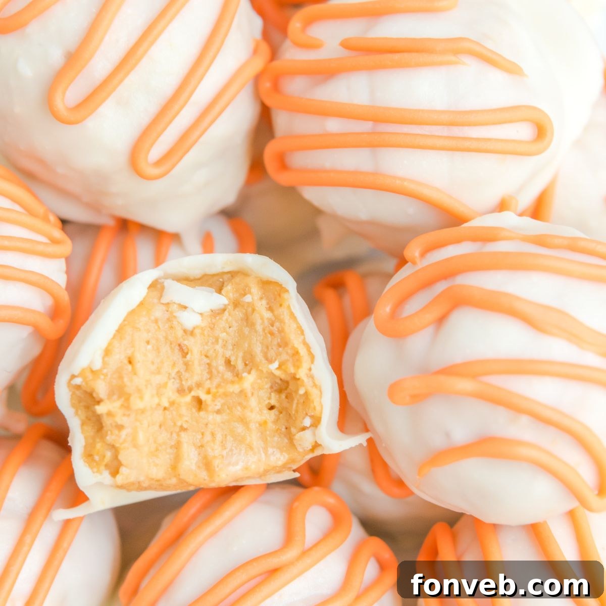 A perfectly formed white chocolate pumpkin truffle with a bite taken out, showcasing the smooth, spiced interior.