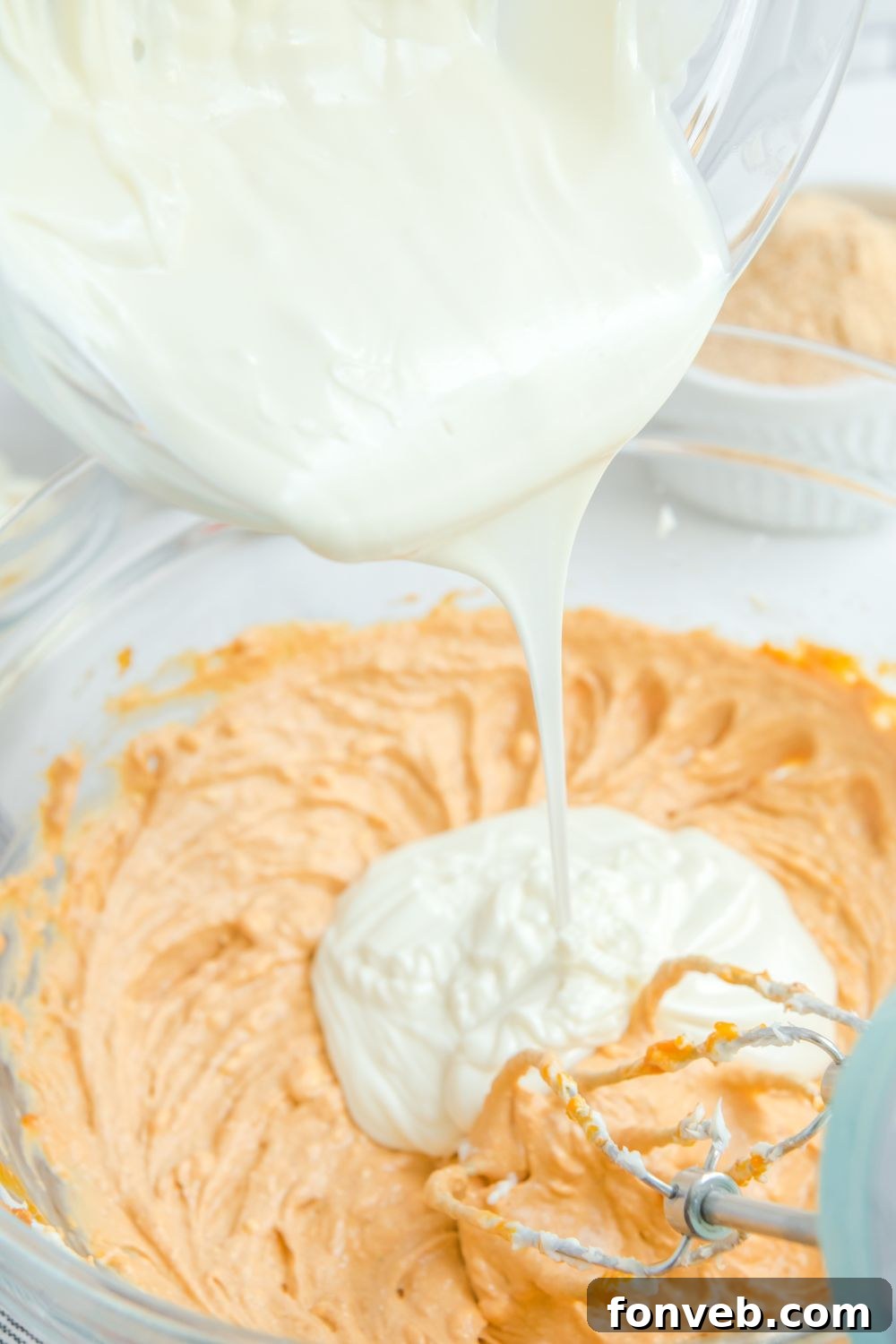 Melted white chocolate being stirred into the pumpkin mixture in a bowl.