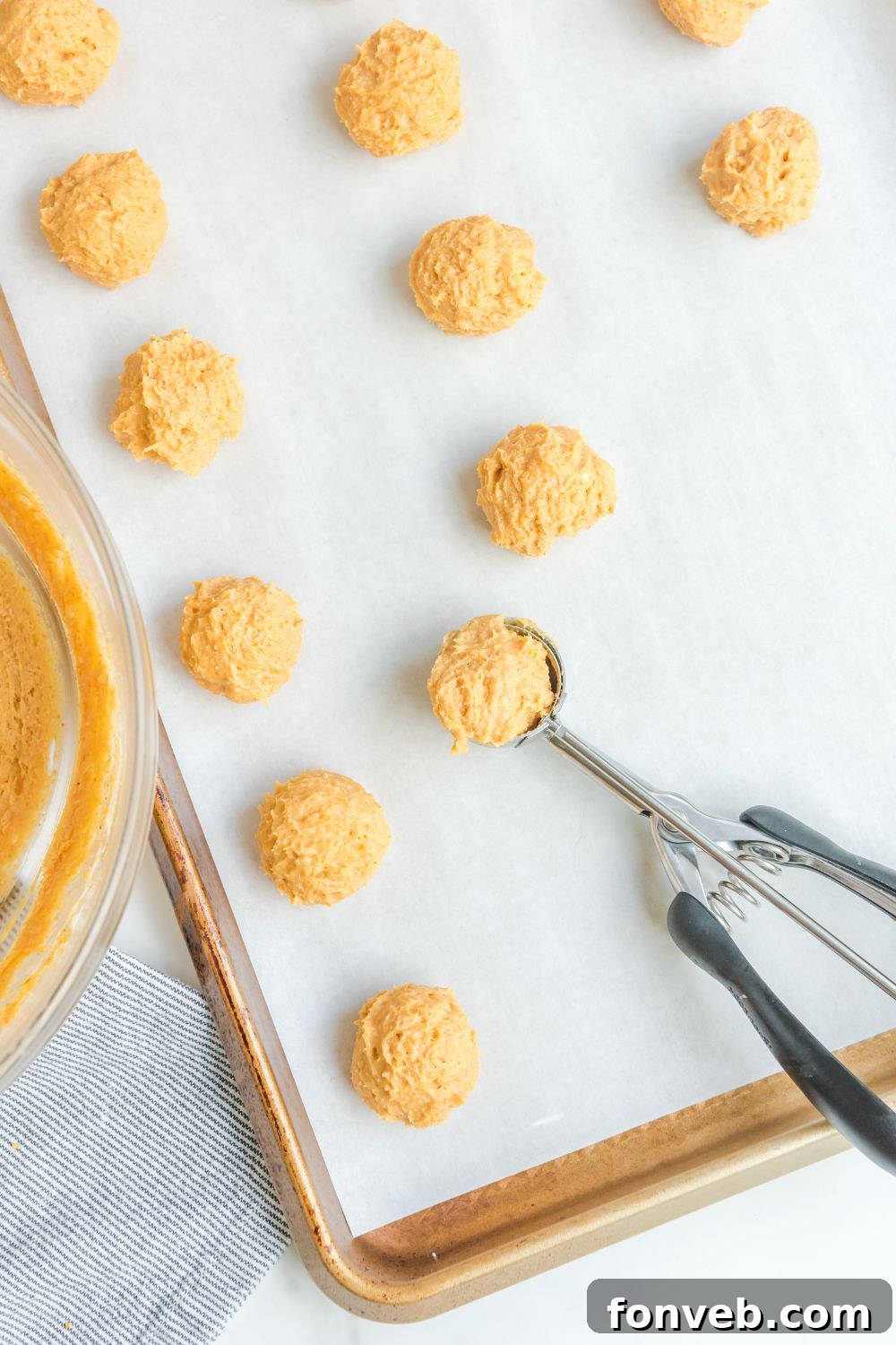 A perfectly rounded pumpkin truffle ball resting on a cookie scoop, ready for chilling.