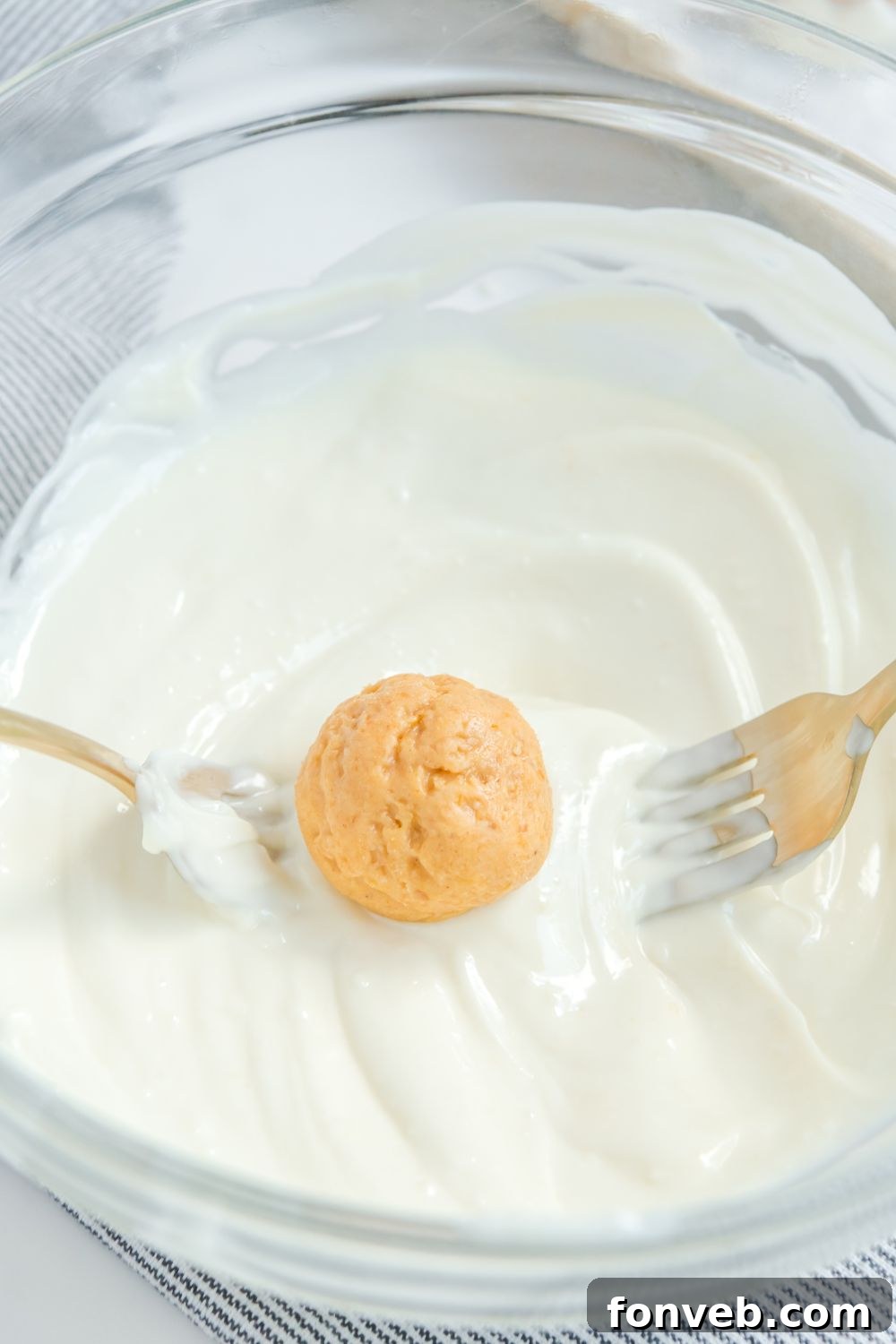 A pumpkin truffle ball being carefully dipped and coated in smooth white chocolate.