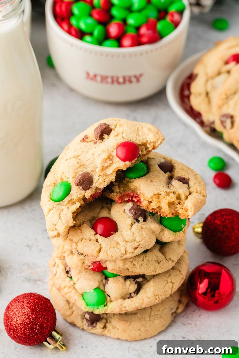 Festive M&M Delights 13 A stack of golden-brown Christmas M&M cookies on a table, with one cookie cut in half to reveal its soft, chewy interior