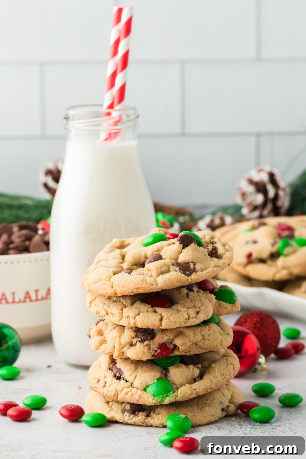 Festive M&M Delights 16 Christmas M&M cookies artfully arranged on a table with a jug of milk in the background, ready for serving, showcasing a cozy holiday scene