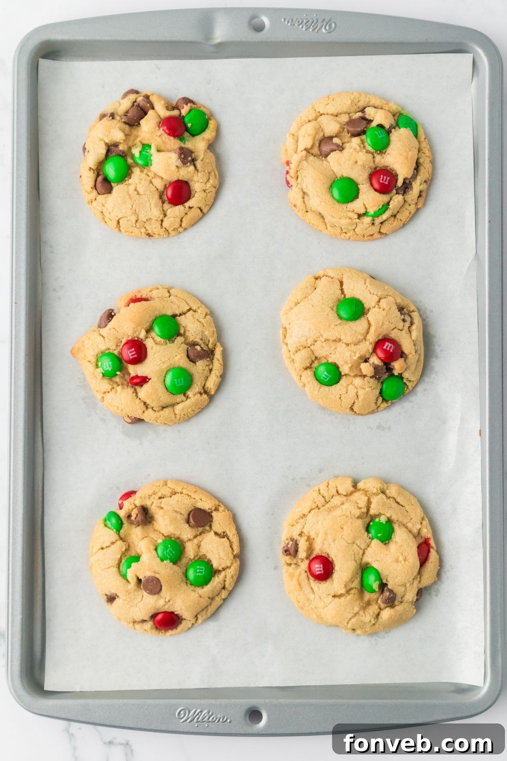 Festive M&M Delights 4 Baked Christmas M&M cookies cooling on a wire rack over a baking tray, showcasing their perfect round shape and colorful candies