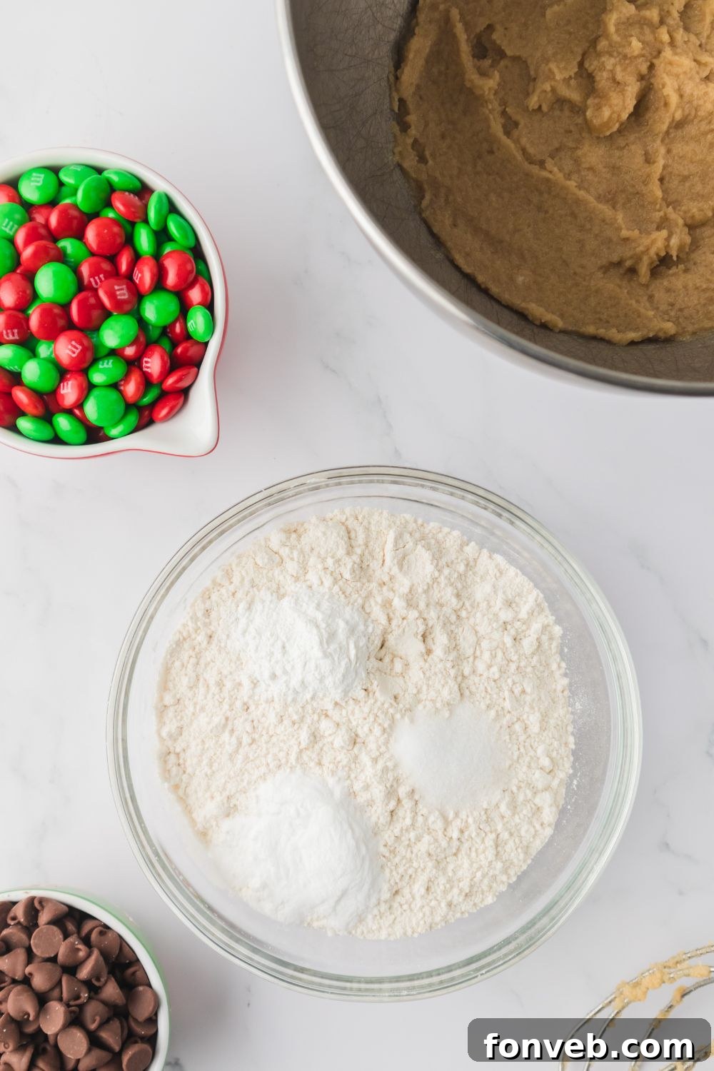 Festive M&M Delights 6 Dry ingredients including flour, salt, baking soda, and baking powder in a bowl, surrounded by other cookie ingredients