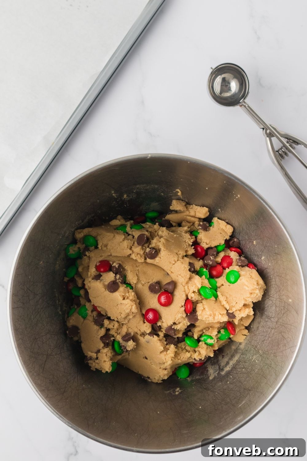 Festive M&M Delights 9 Chocolate chips and M&Ms sprinkled on top of cookie dough in a mixer bowl, ready to be folded in
