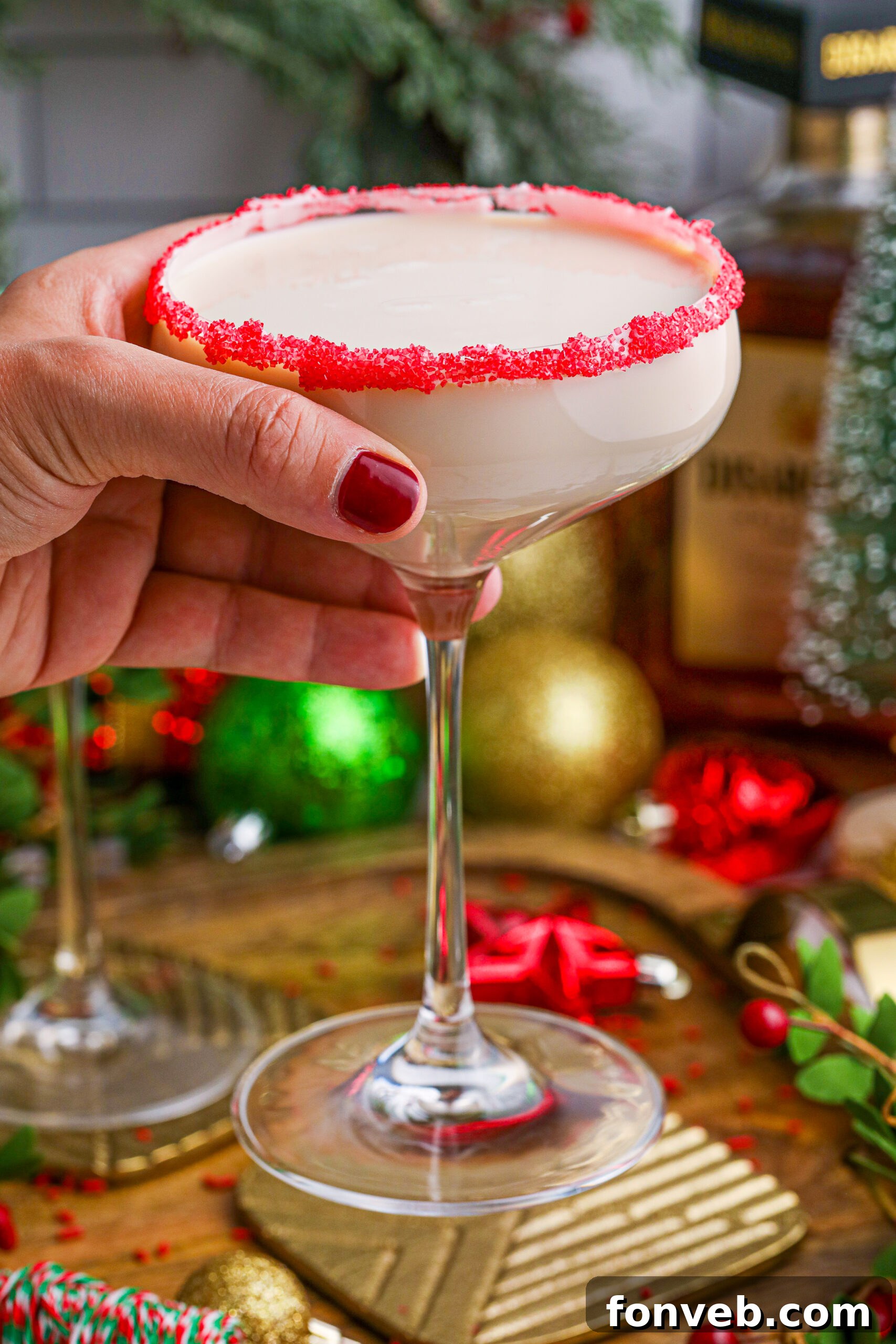 A hand holding a glass of Sugar Cookie Cocktail, showcasing its vibrant red sugar rim and creamy texture, ready to be enjoyed.
