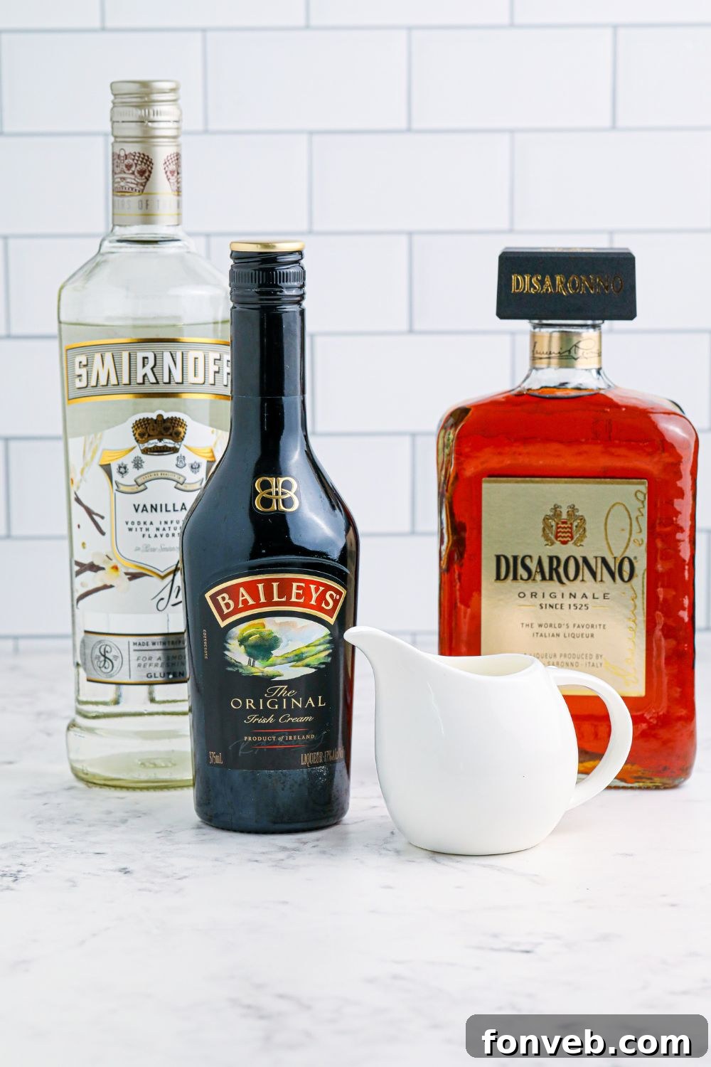 A collection of ingredients for a Baileys cocktail, including bottles of Baileys, Amaretto, and vanilla vodka, neatly arranged on a table.