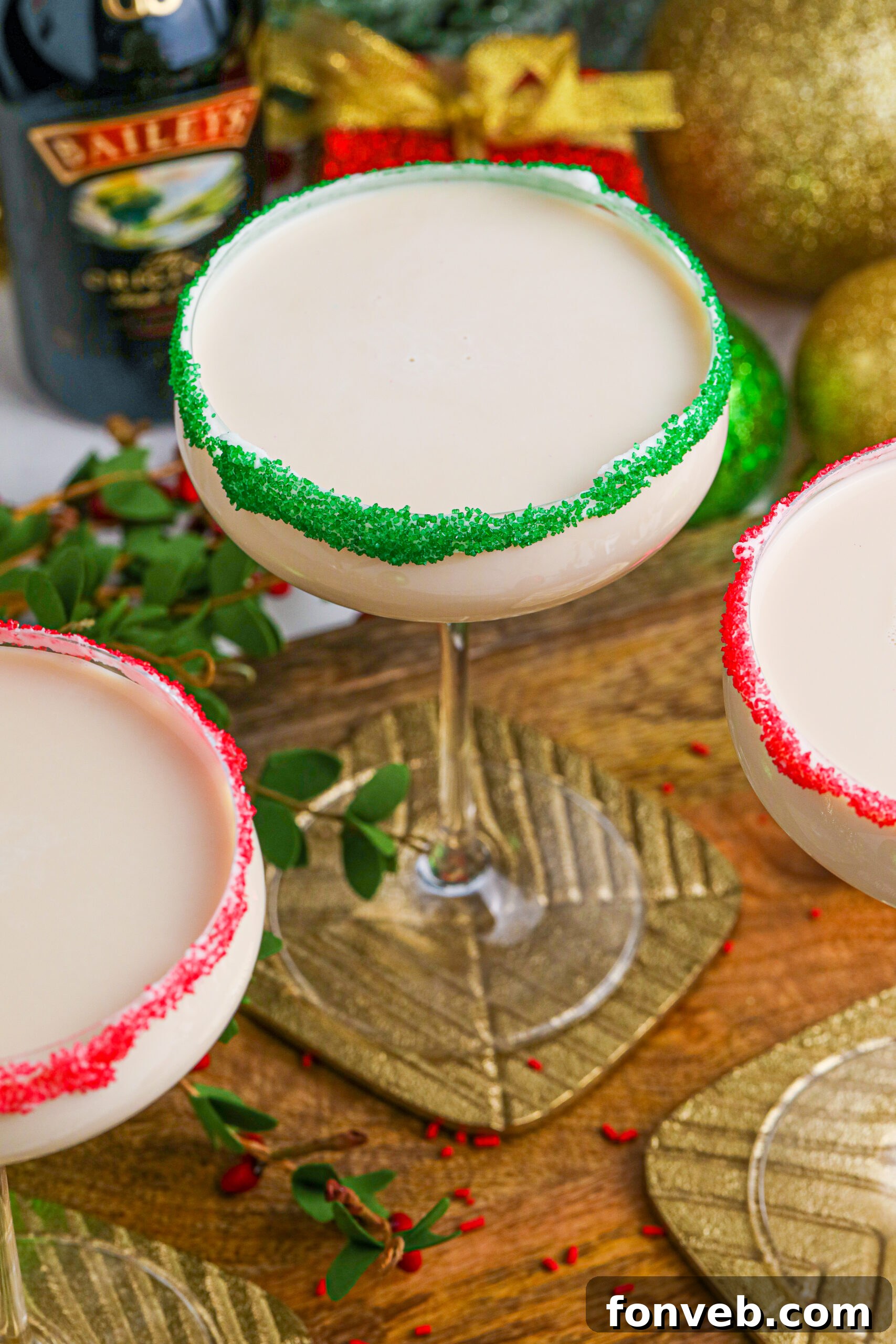 A trio of Sugar Cookie Cocktails in elegant glasses, adorned with festive red and green sugar rims, ready to be served on a wooden table.
