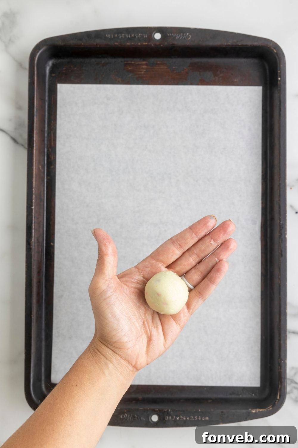 rolled truffle dough in hand above a metal baking tray 
