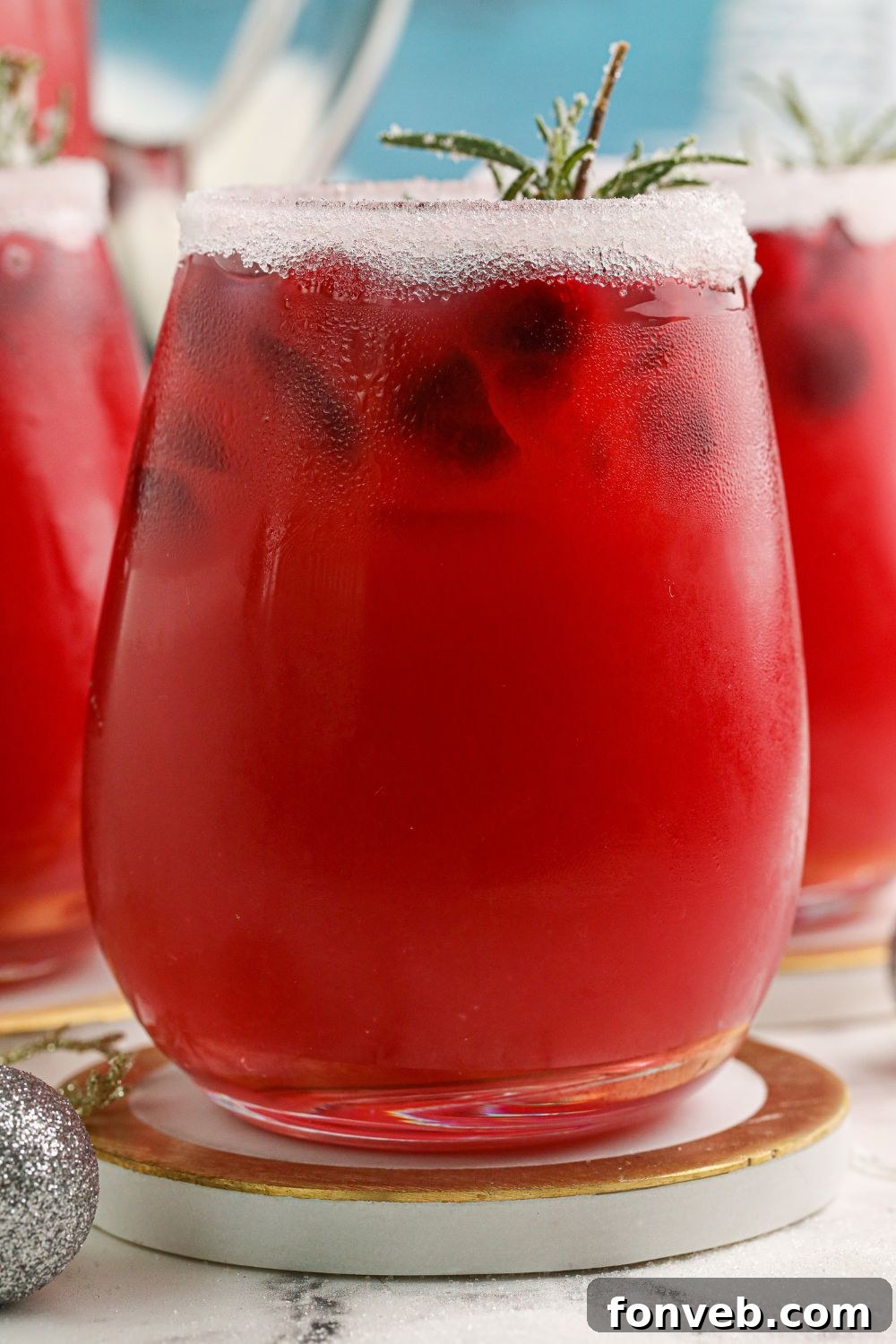 Mistletoe Magic Margarita 12 A side view of a glass filled with a cranberry cocktail, resting on a coaster on a table.