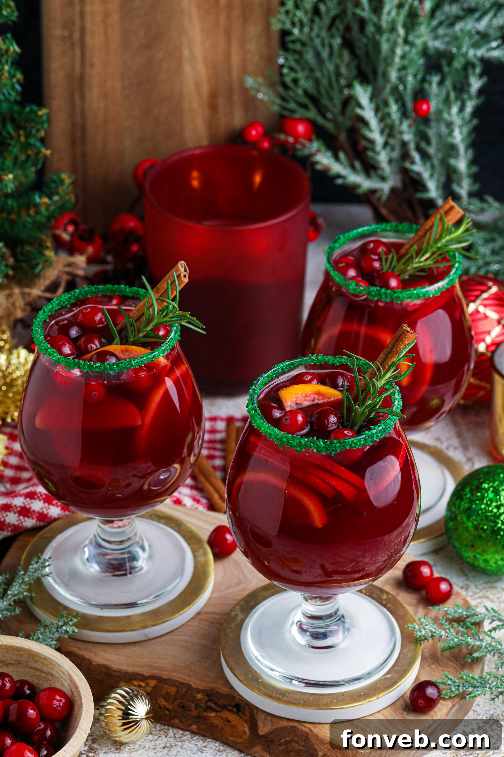 A photo of red christmas sangria in clear glasses with a green sugar rim on a wood table