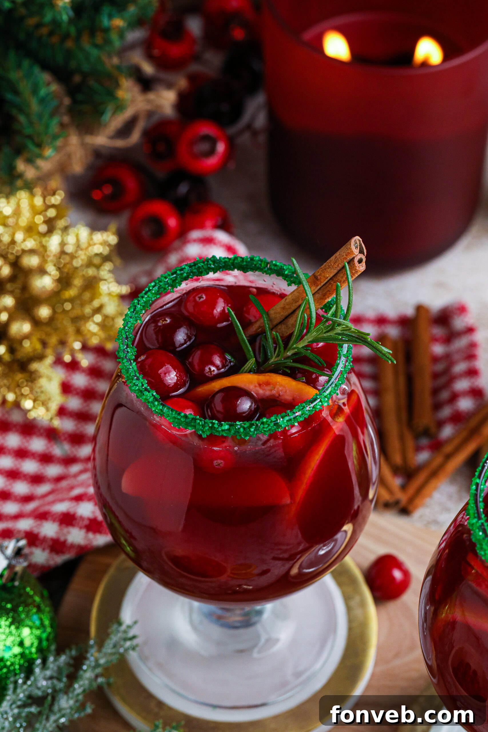 up close shot of red christmas sangria in a clear glass with a green sugar rim on a wood table with a candle lit in the background