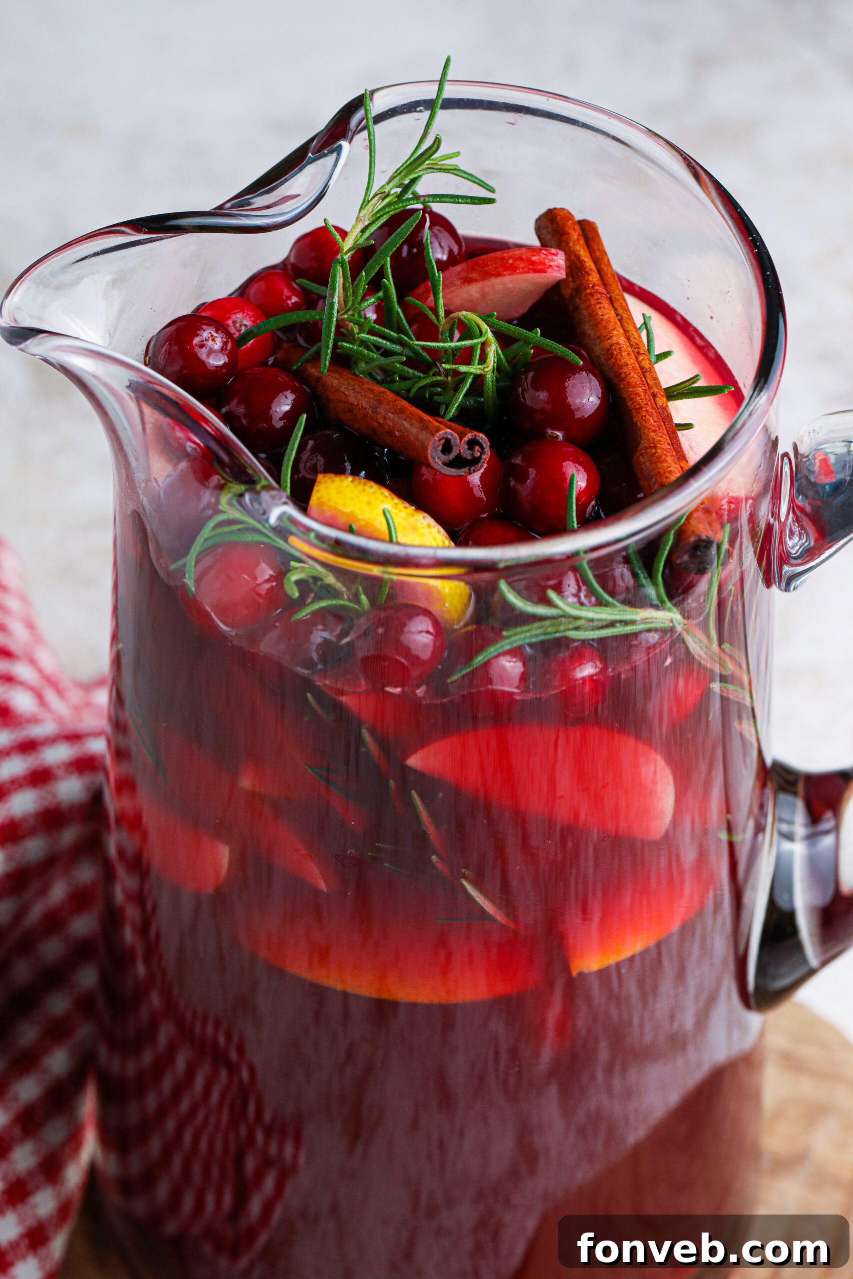up close shot of red christmas sangria in a large glass clear pitcher filled with cranberries and cinnamon sticks