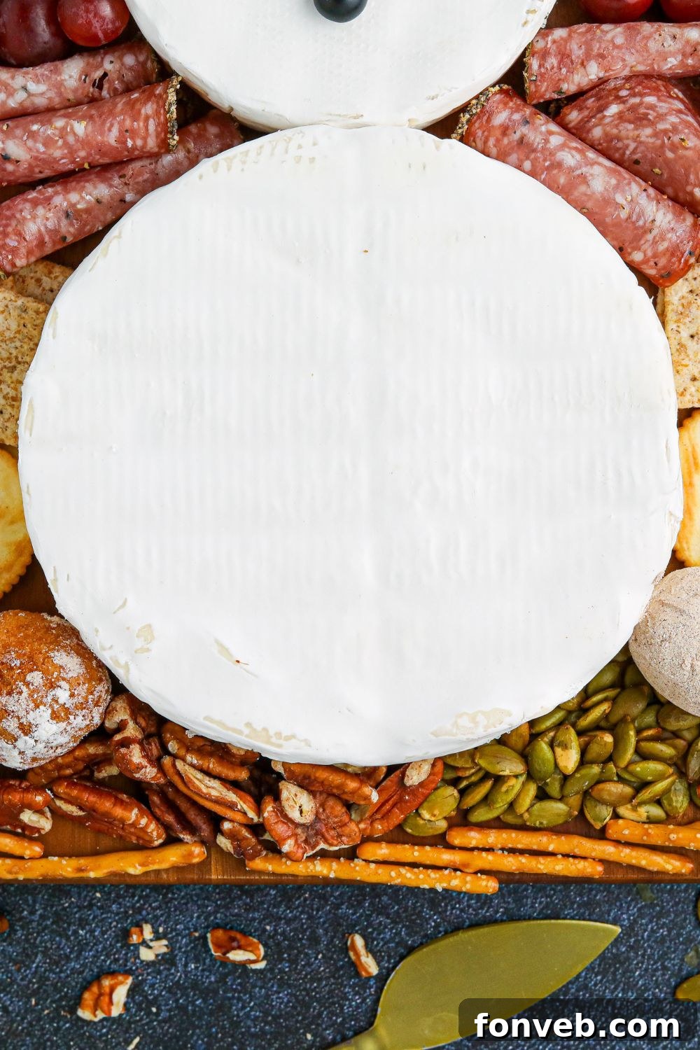 Close up view of a brie cheese wheel on a serving tray, adorned with dried fruit to form part of the snowman's face