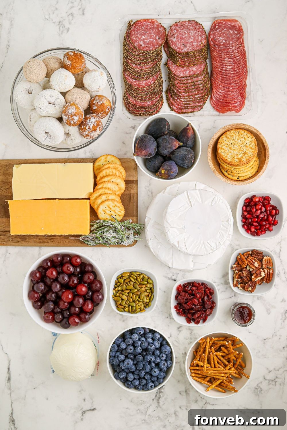 Assortment of ingredients for Snowman Charcuterie Board laid out on a table: cheeses, crackers, meats, fruits, and pretzels