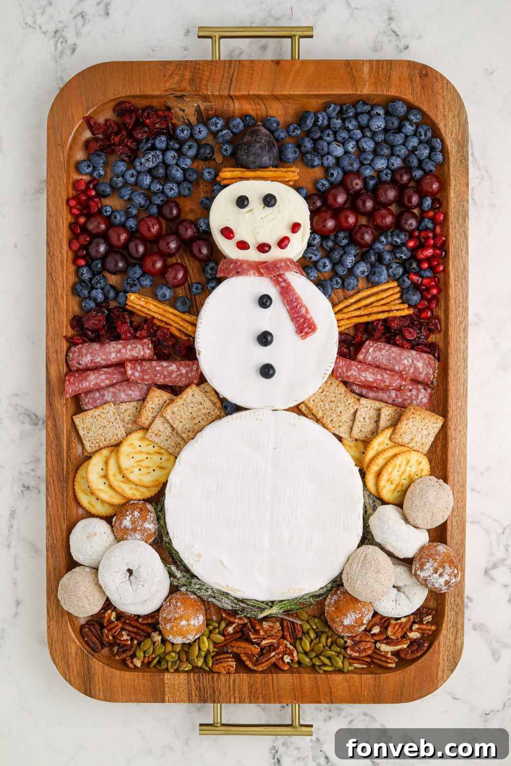 Final stages of assembly of Snowman Charcuterie Board, with various snacks being added around the cheese snowman