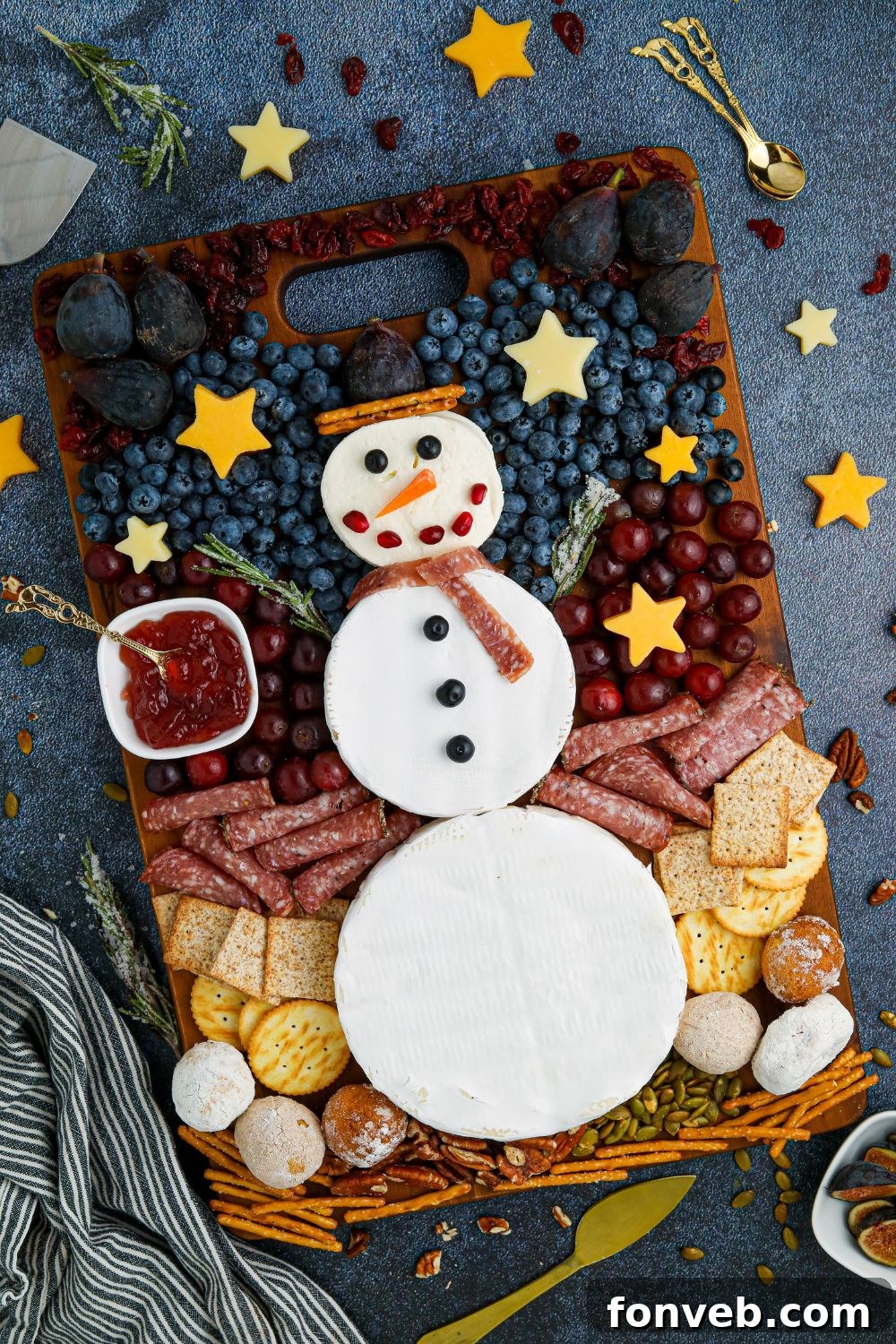 Finished snowman snack tray on a table, with diverse snacks arranged around the cheese snowman