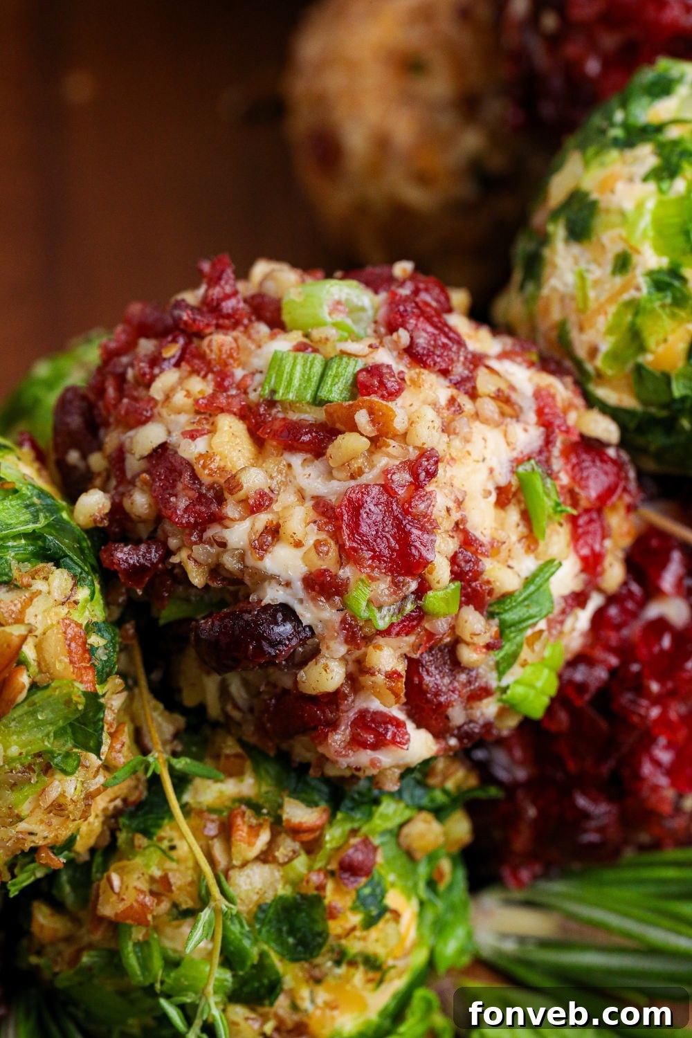 Close-up stack of various mini cheese balls on a wooden table, displaying different coatings and colors.