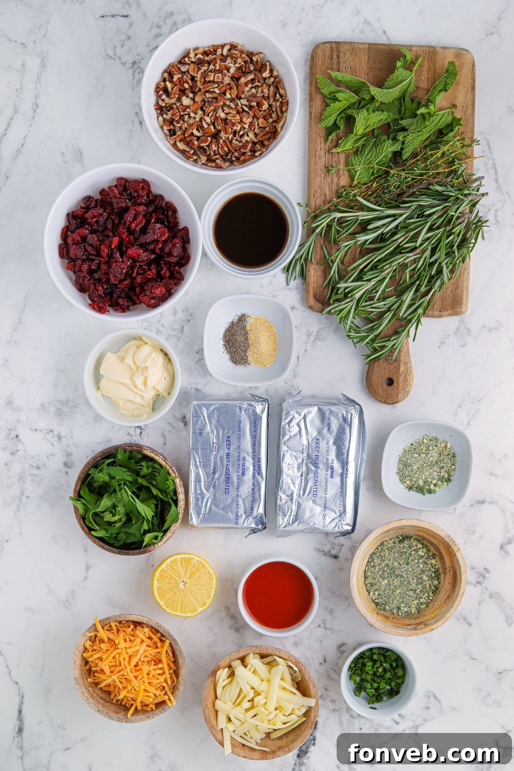 Assortment of fresh ingredients for a cheese ball wreath laid out on a marble counter, including cream cheese, herbs, and spices.