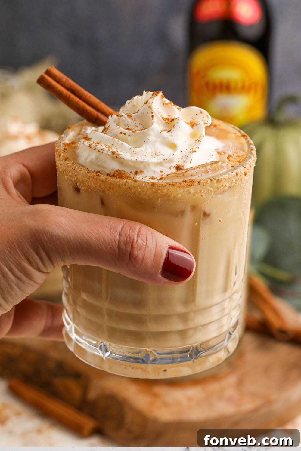 A hand gently holds a glass filled with a creamy pumpkin white russian, showcasing its inviting color and texture.