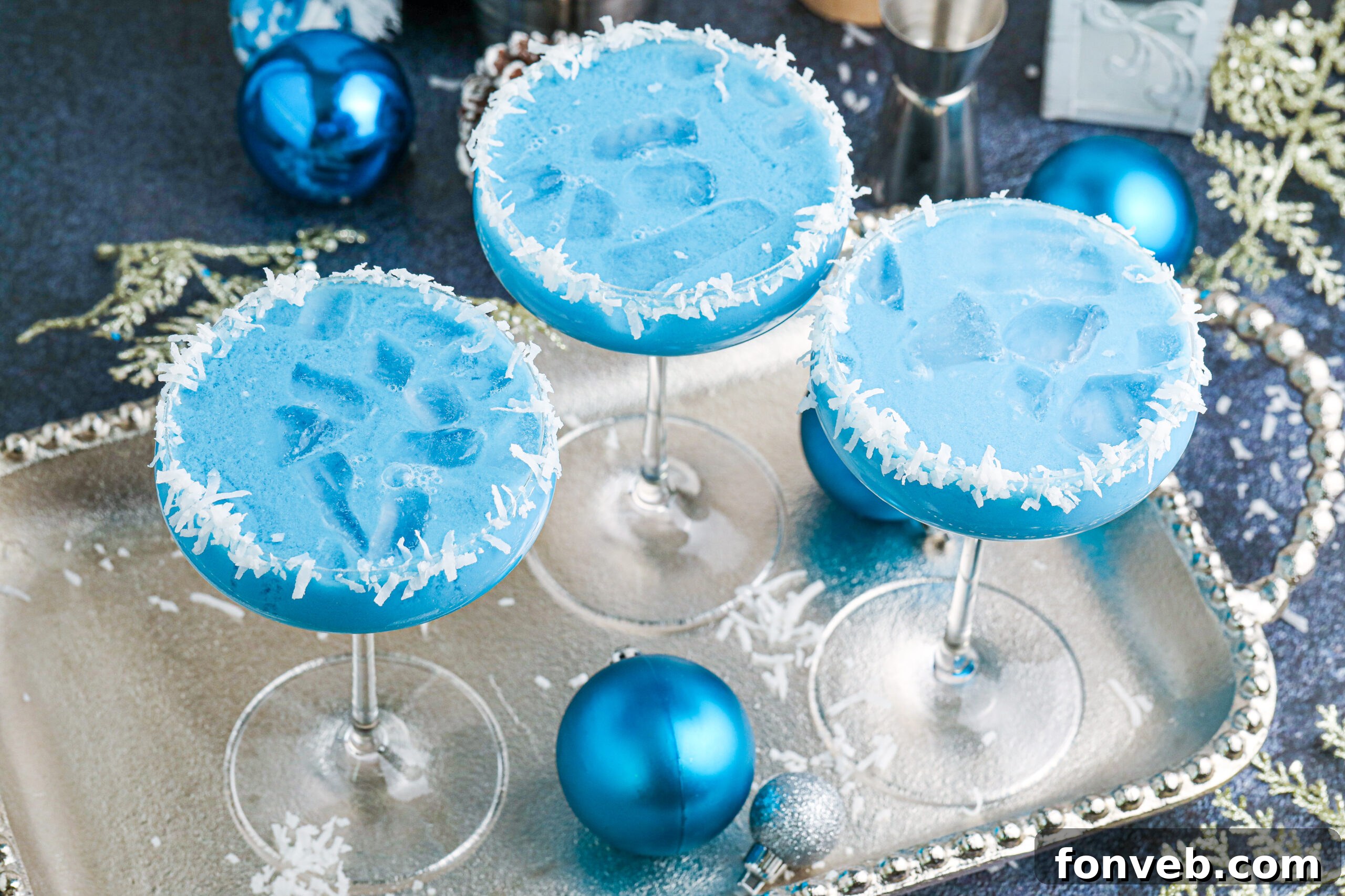 Multiple blue Christmas cocktails glistening on a silver platter, reflecting festive lights
