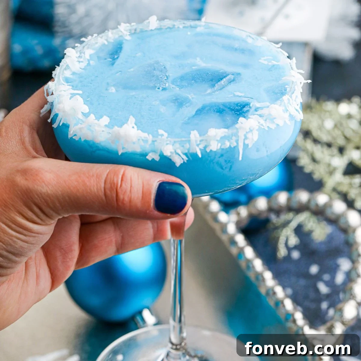 Close-up of a hand holding a sparkling Blue Christmas Cocktail, ready for a festive toast