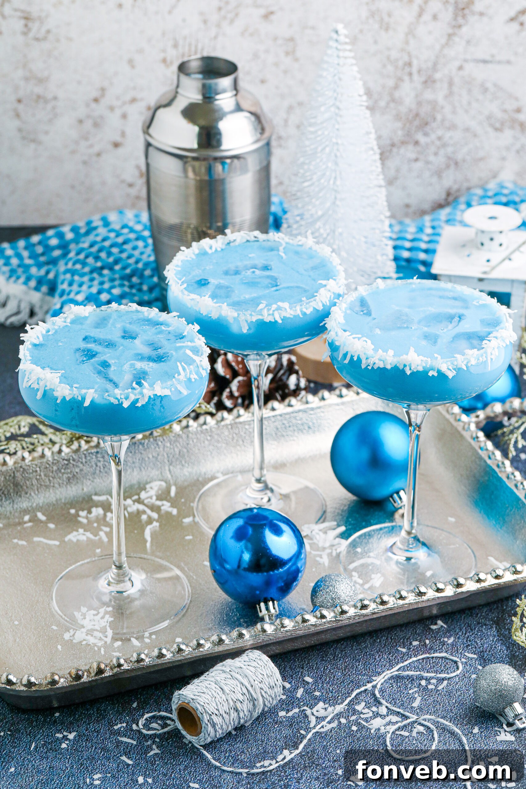 Three exquisite glasses of Blue Christmas Cocktail served on a gleaming silver platter, adorned with holiday decorations