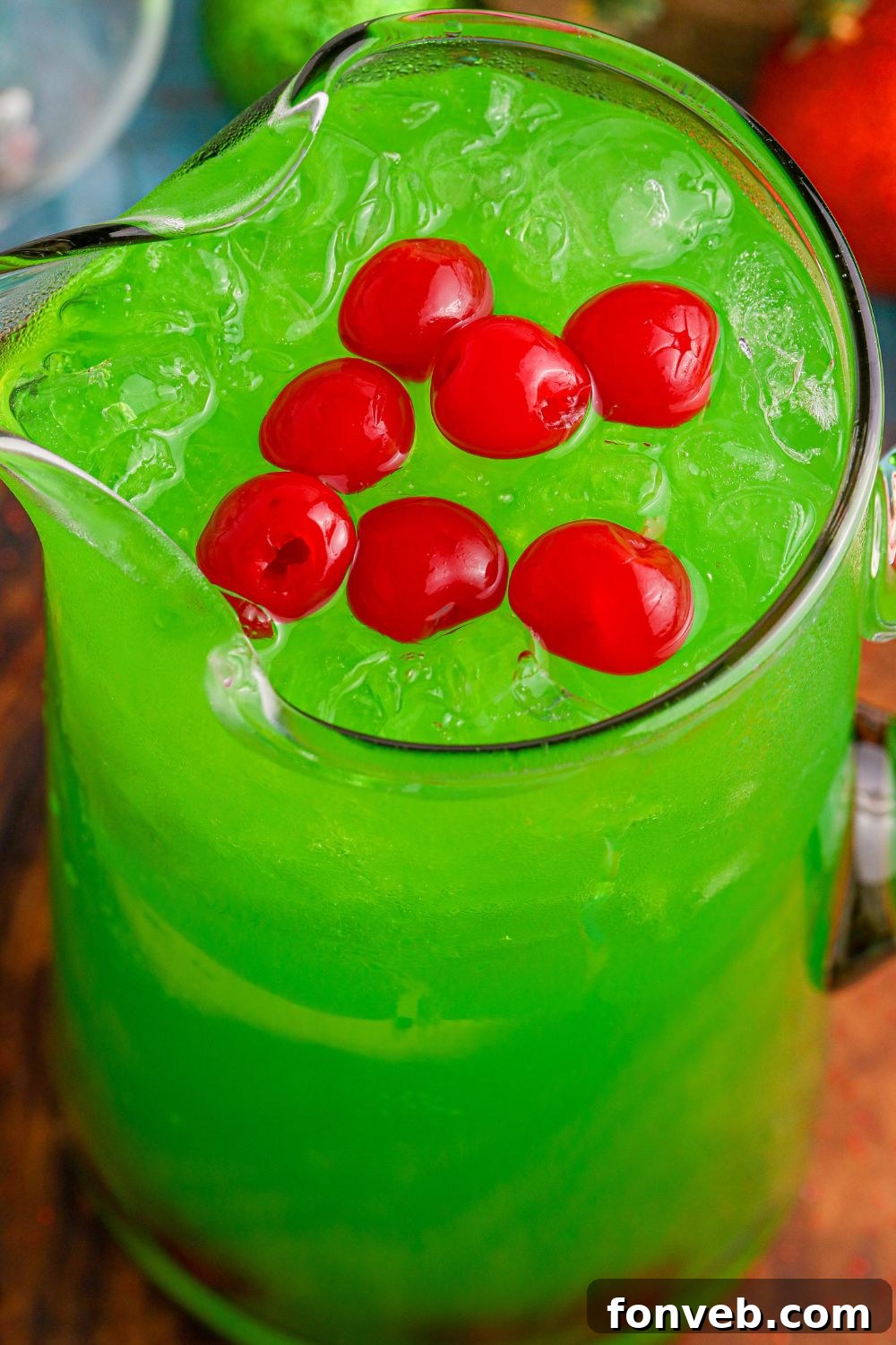 punch in a pitcher with red cherries on top of the green punch in container