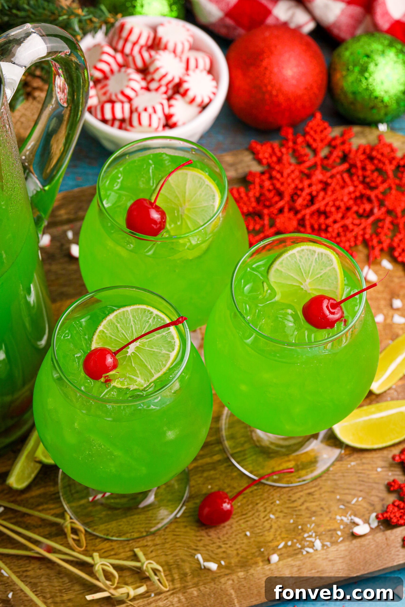 Grinch Punch in a clear glass on a table with a cherry and a lime slice in the glasses, with a bowl of peppermints in the background