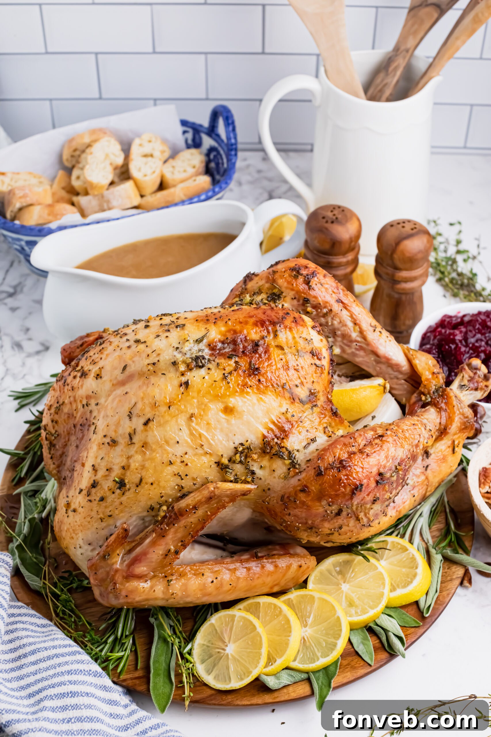 Roasted turkey on a wooden cutting board with gravy in a white bowl and cranberry sauce in another bowl in the background
