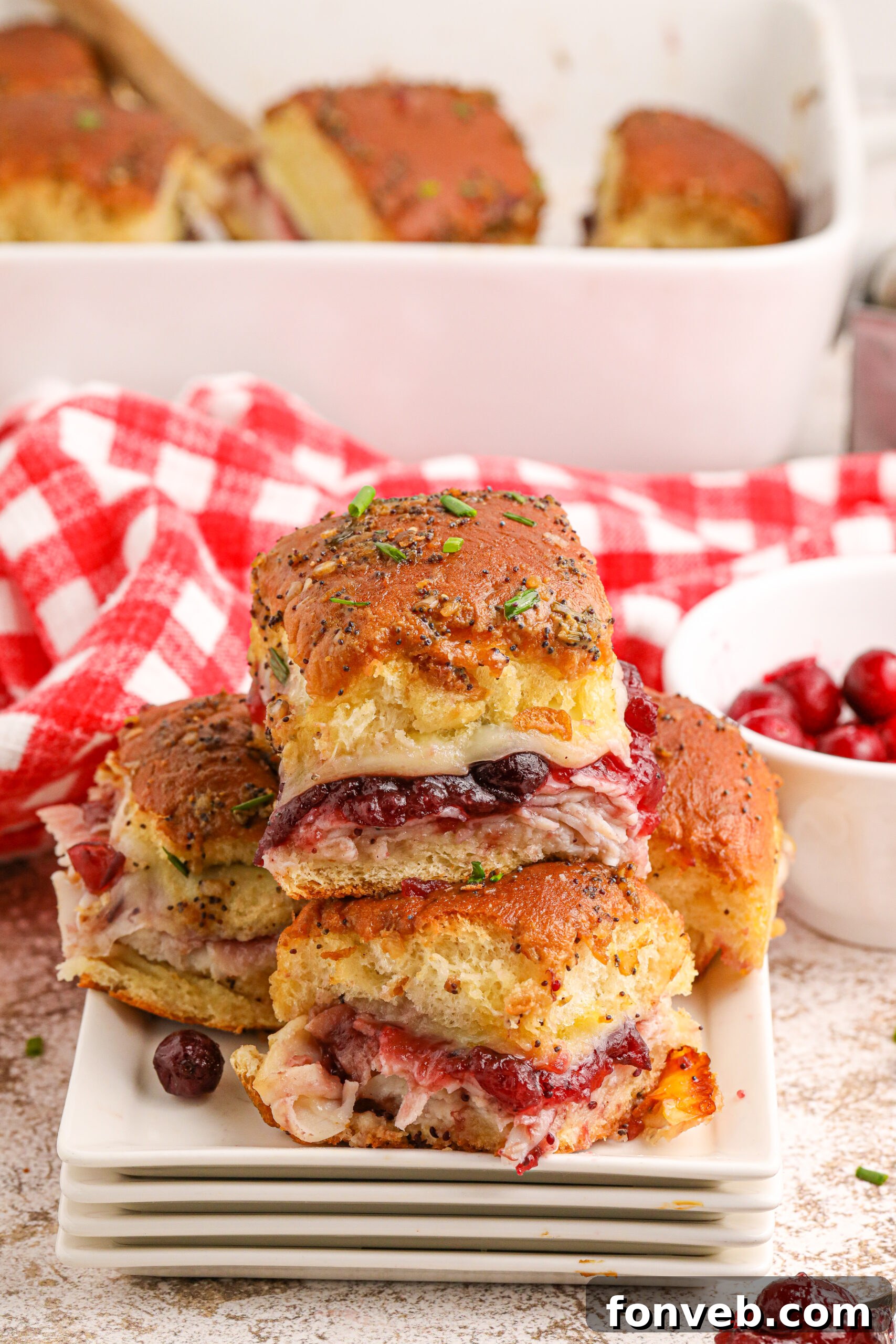 Thanksgiving Sliders stacked on white plates on table, showcasing their delicious layers and golden-brown tops
