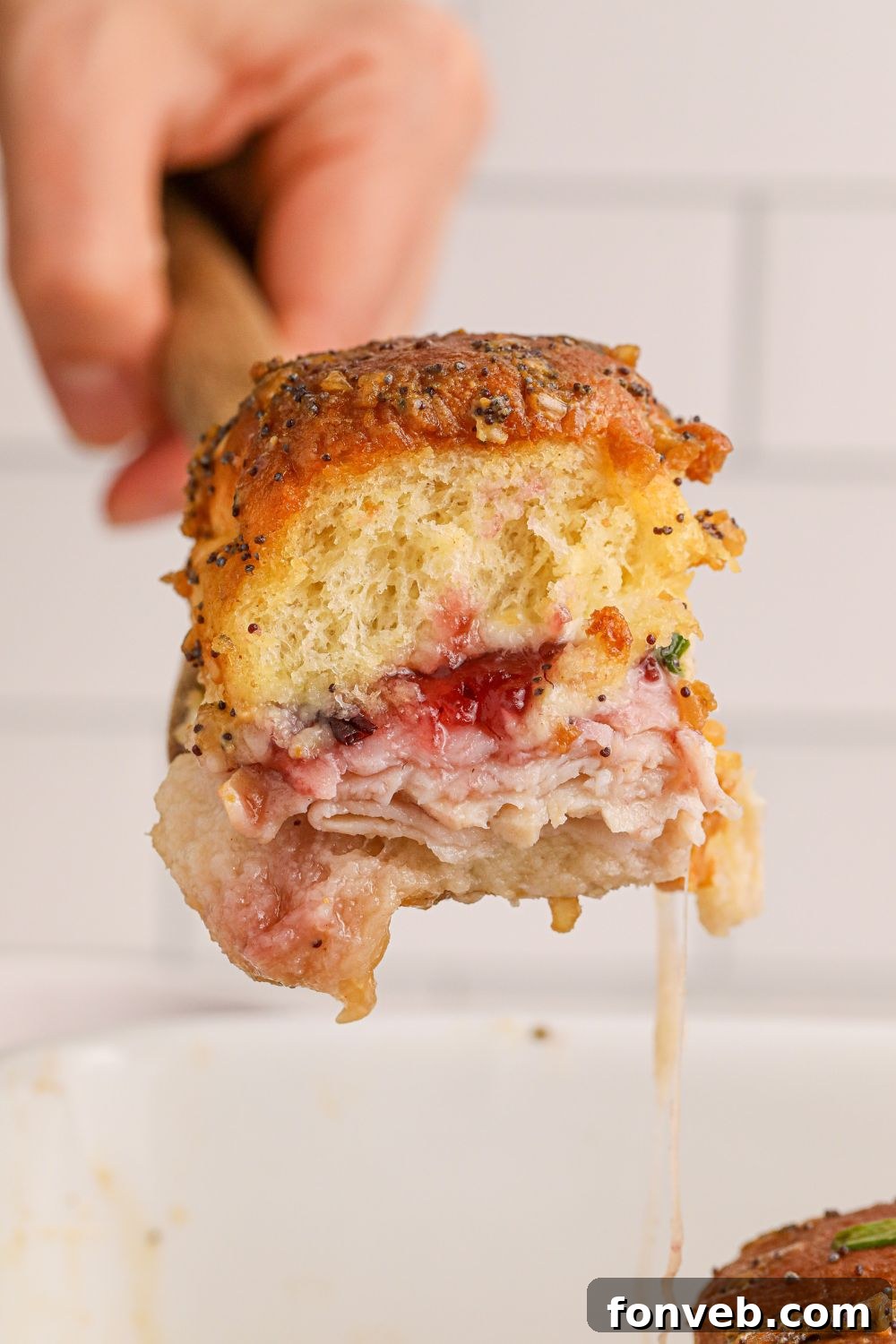 A single Hawaiian slider being lifted from the pan with a spatula, showing the melted cheese and juicy filling