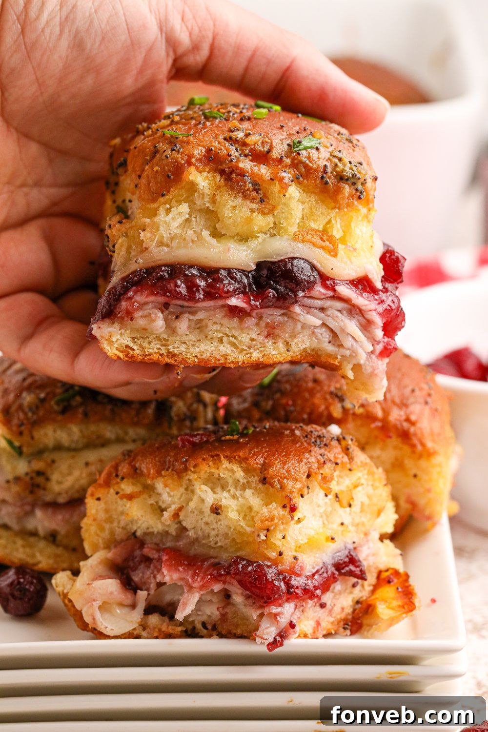 A close-up shot of sliders with deli meat being held, ready to eat