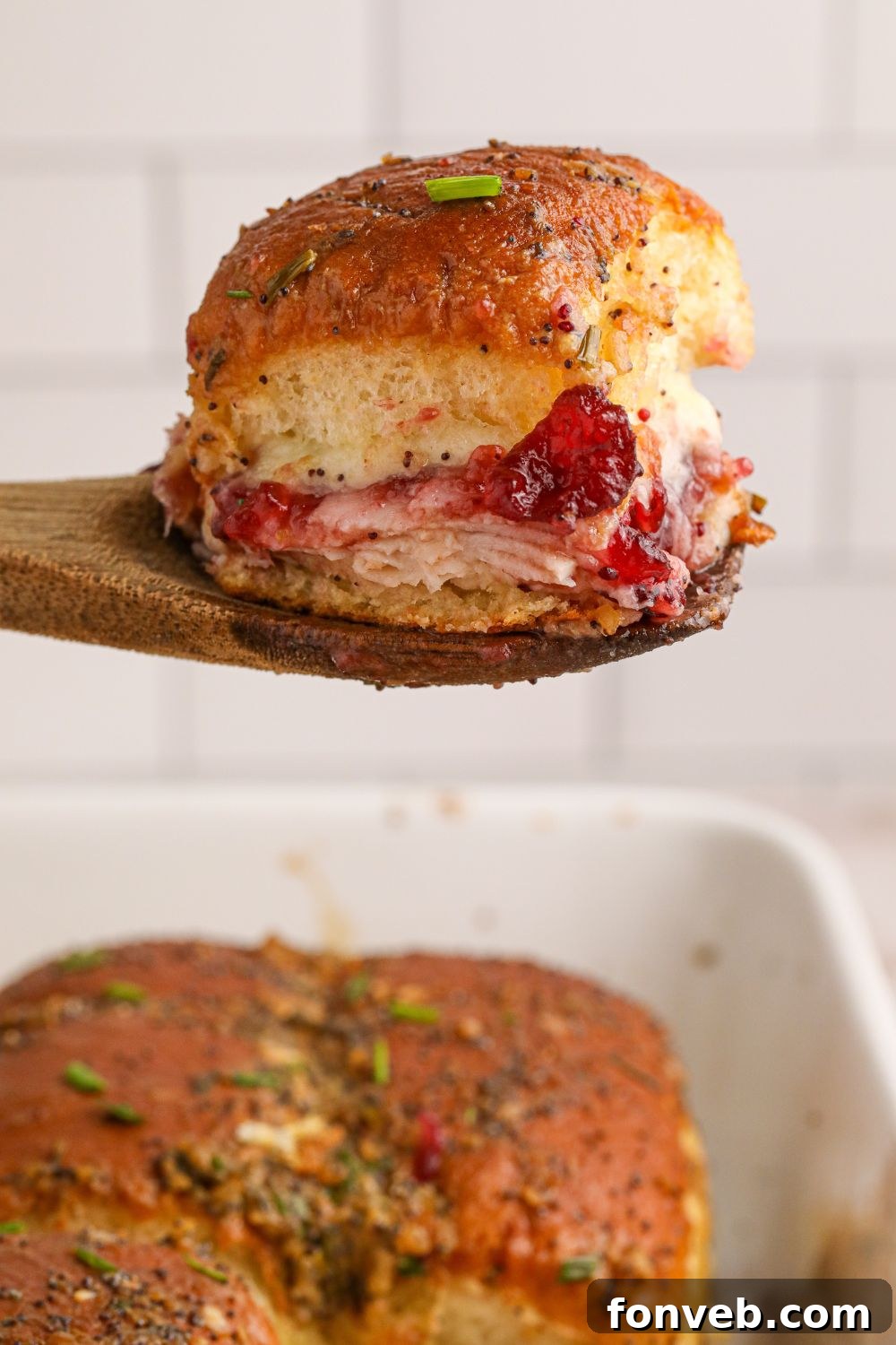 A single turkey slider on a Hawaiian roll being served with a spatula, showing the golden bun and melted cheese