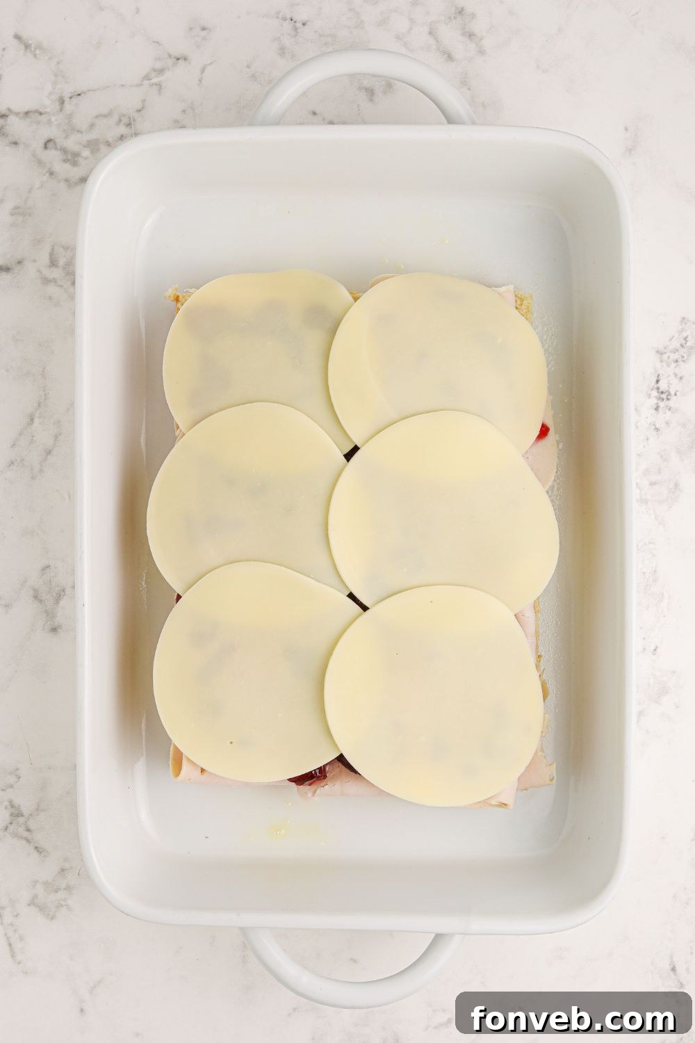 cheese slices covering the turkey and cranberry layers on the sliders