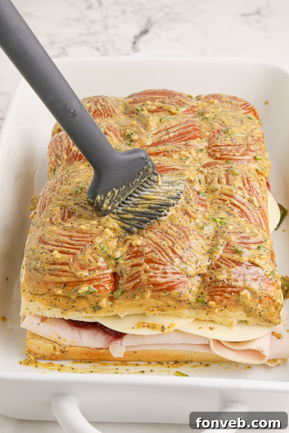 A hand basting slider buns with the savory butter mixture before baking