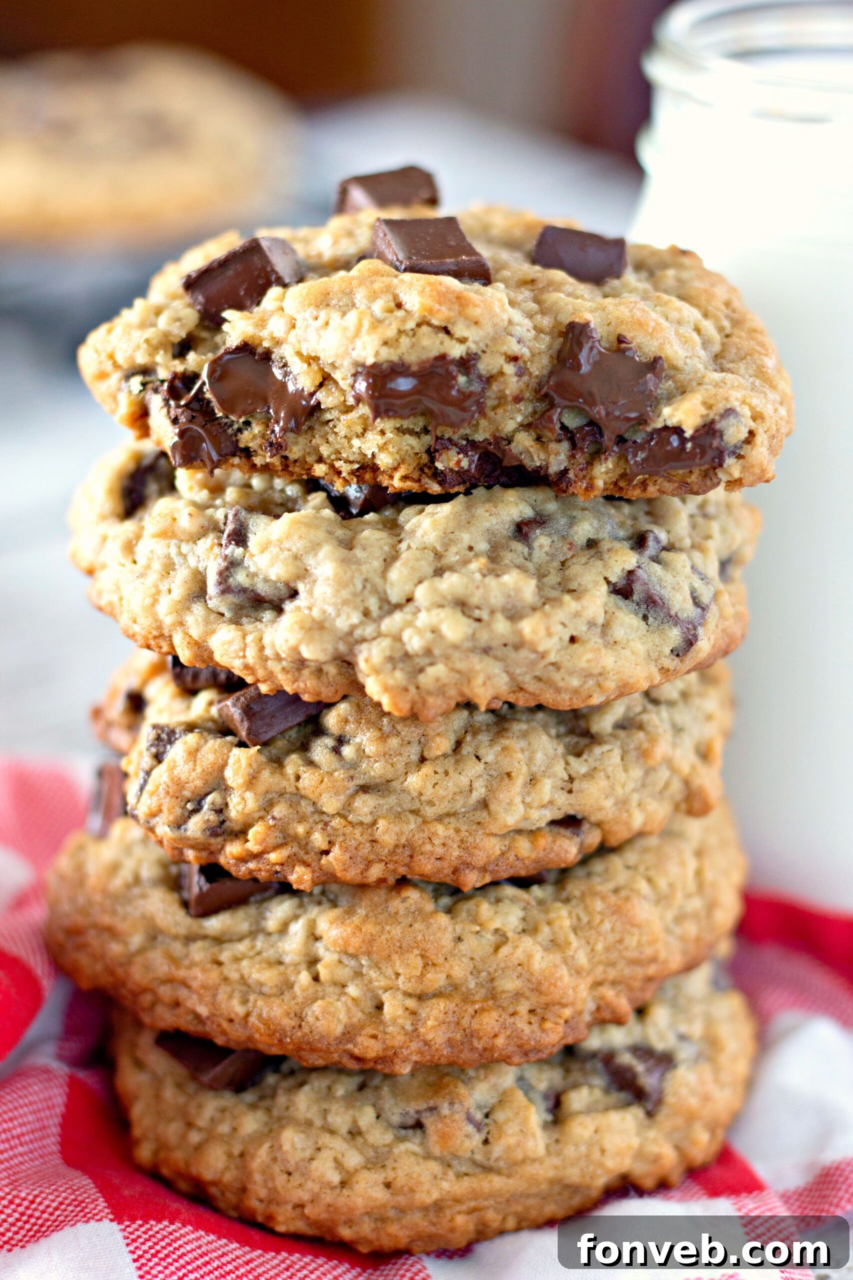 A tempting stack of golden-brown chocolate chunk cookies sits on a rustic wooden table, accompanied by a refreshing glass of milk, showcasing their rich texture and perfect thickness.