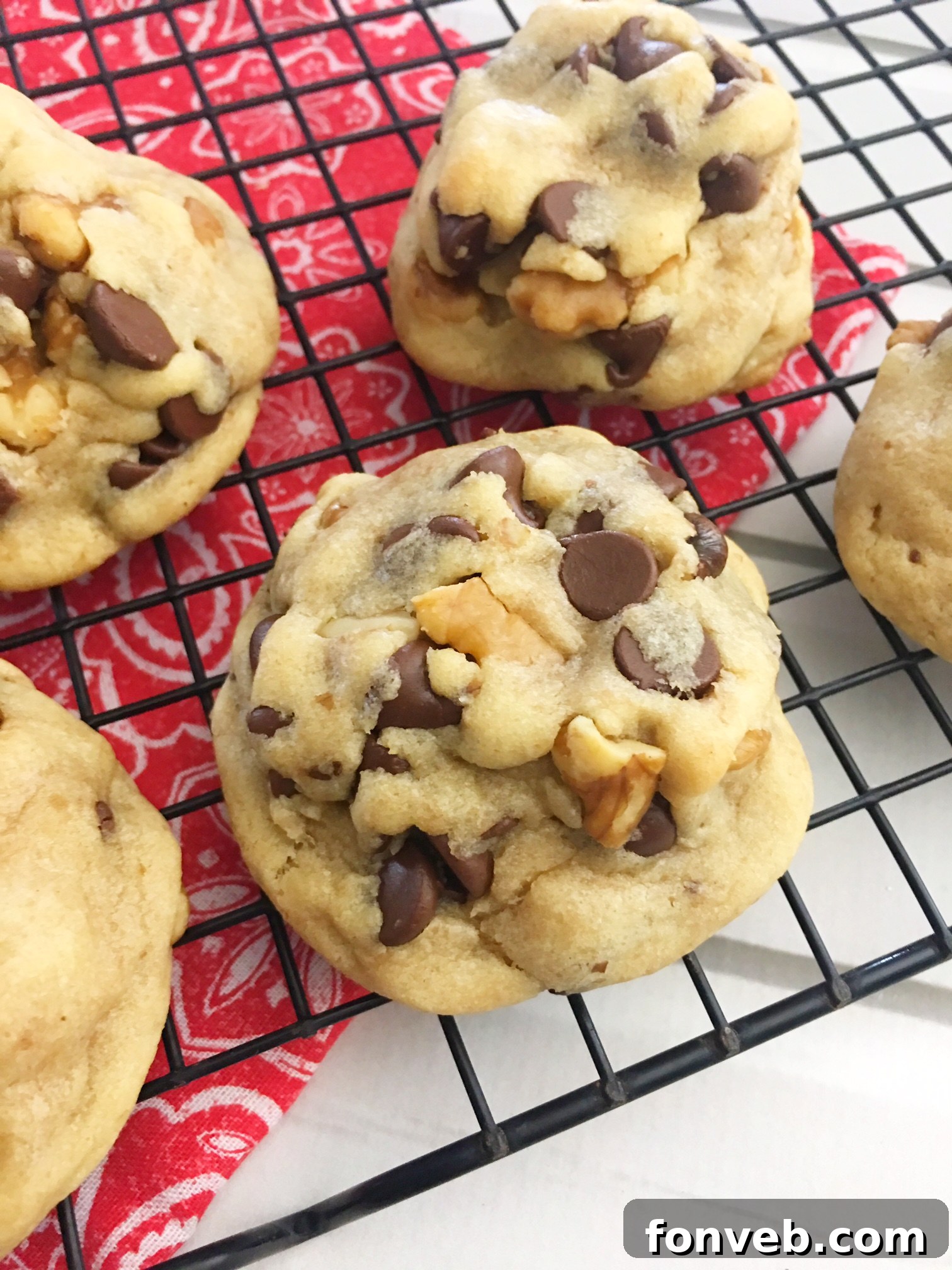 A tray of freshly baked, golden-brown chocolate chip cookies cools on a table, their irregular shapes and melted chips inviting a taste.