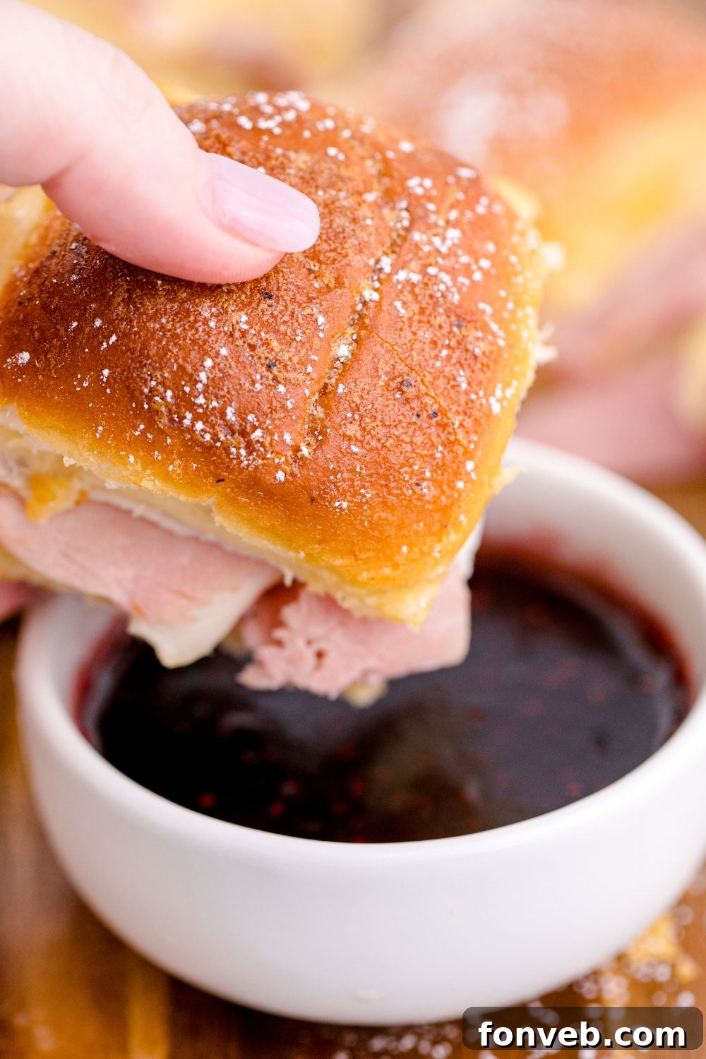 A Monte Cristo Slider held above a small white bowl of jam, ready for dipping.