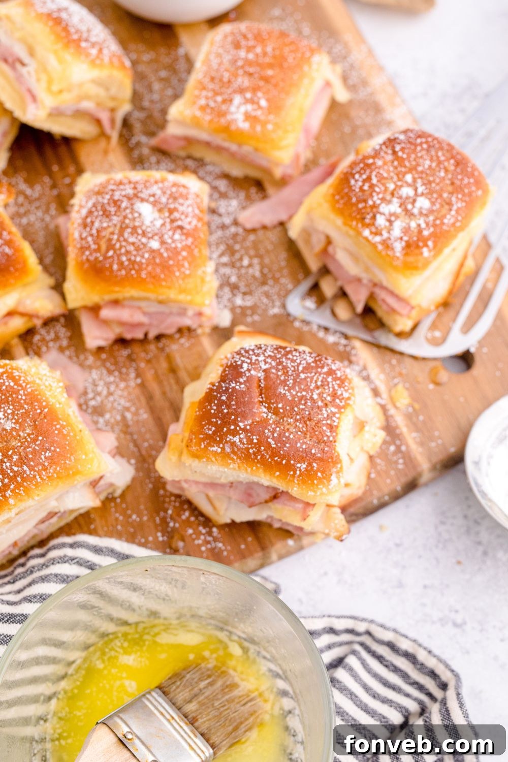 Monte Cristo Sliders arranged on a cutting board, surrounded by fresh ingredients and a jar of jam.