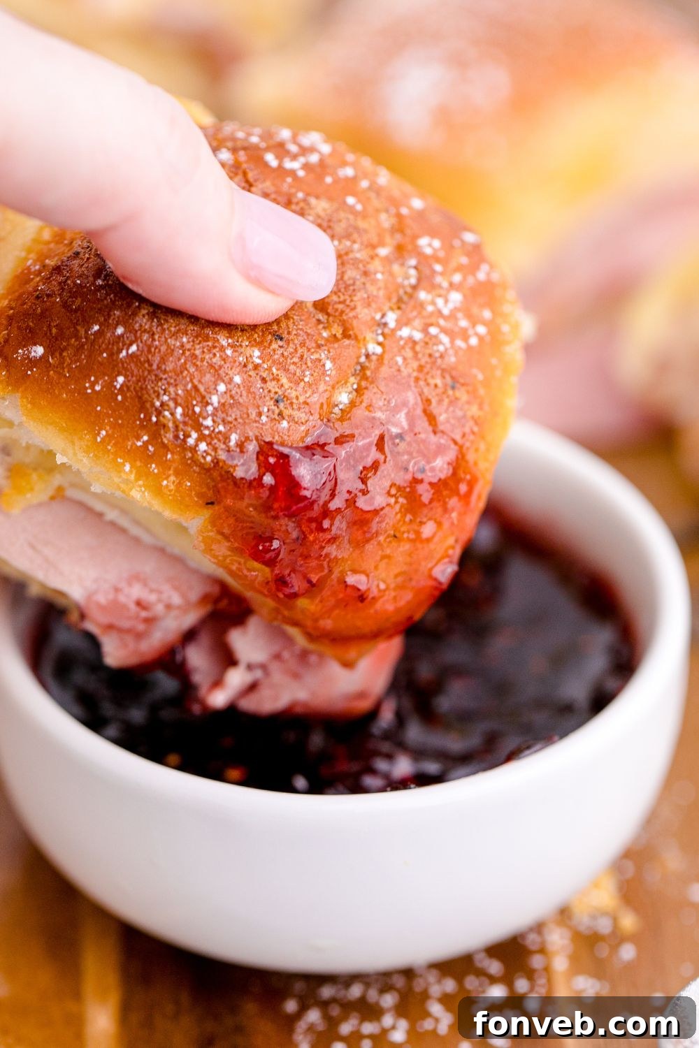 A Monte Cristo Slider being dipped into a bowl of fruit jam on a table.