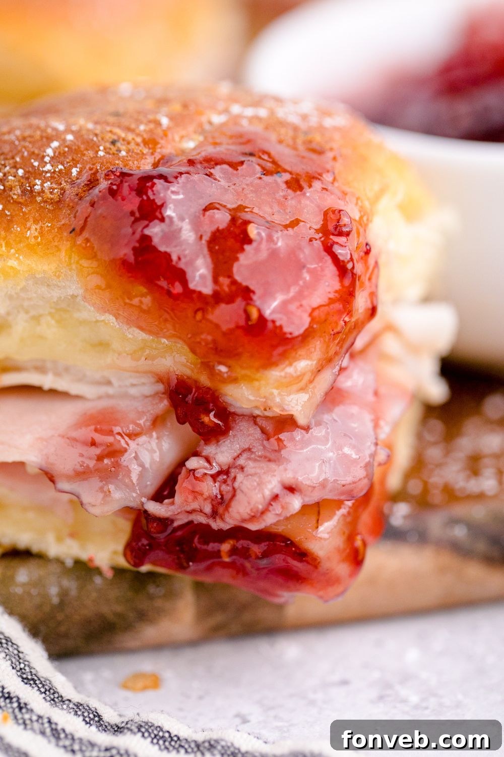 A Monte Cristo Slider being dipped into a bowl of vibrant red jam.