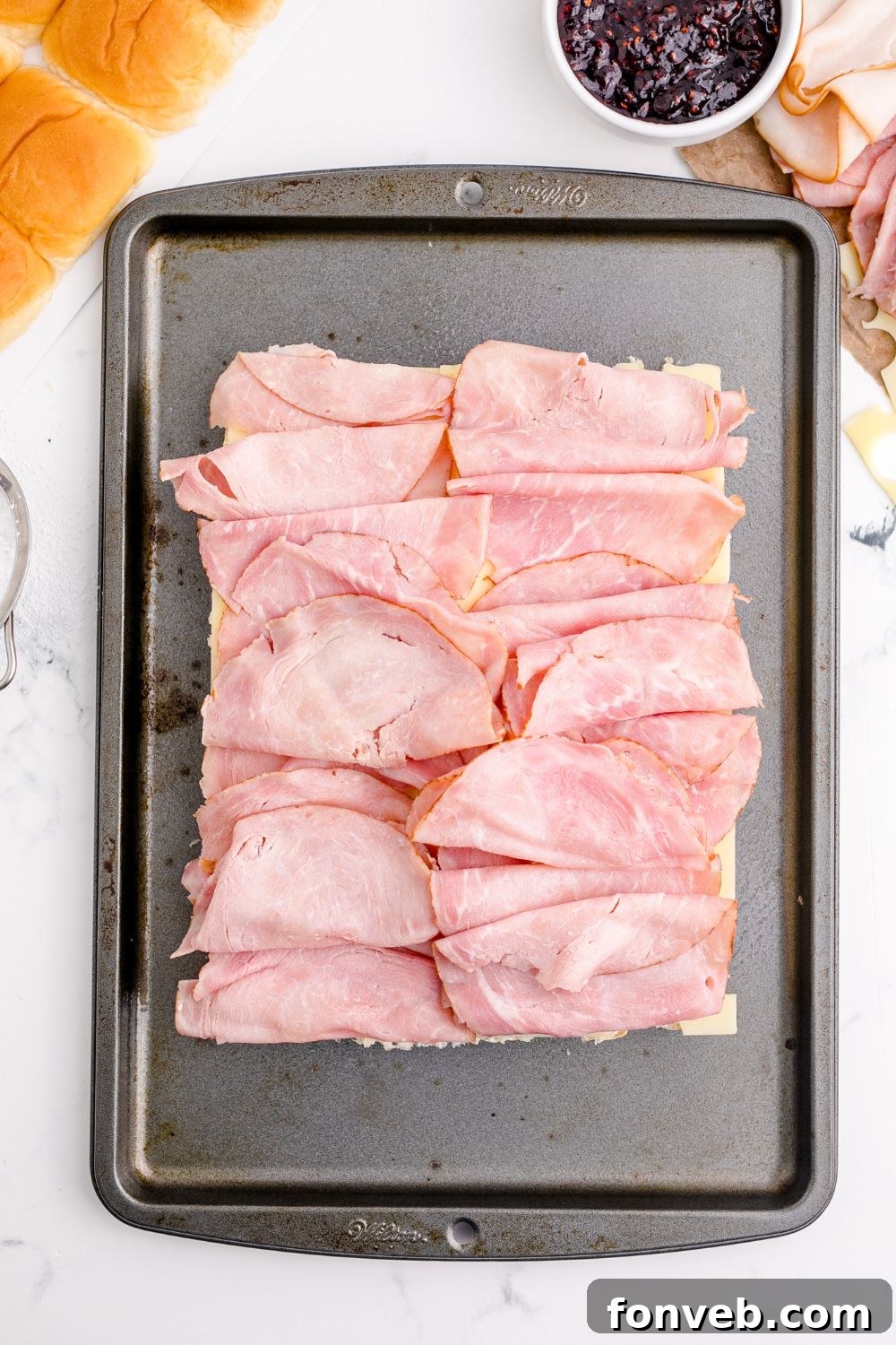 Thinly sliced ham stacked neatly on the bottom halves of slider buns.