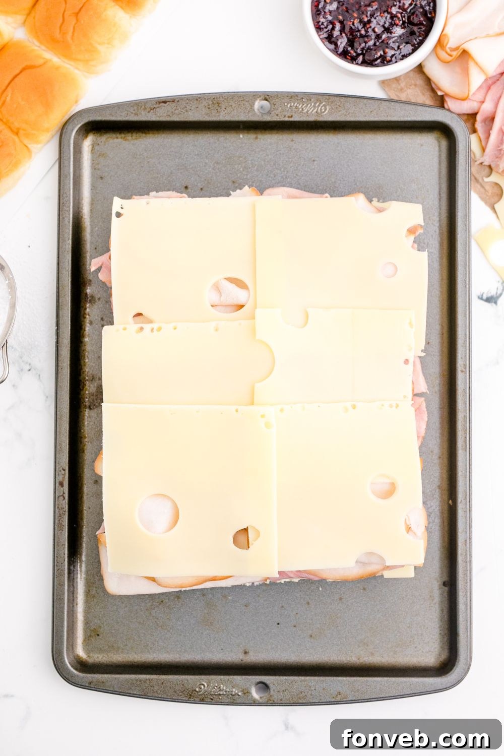 Slices of Swiss cheese covering the turkey and ham on the slider buns.