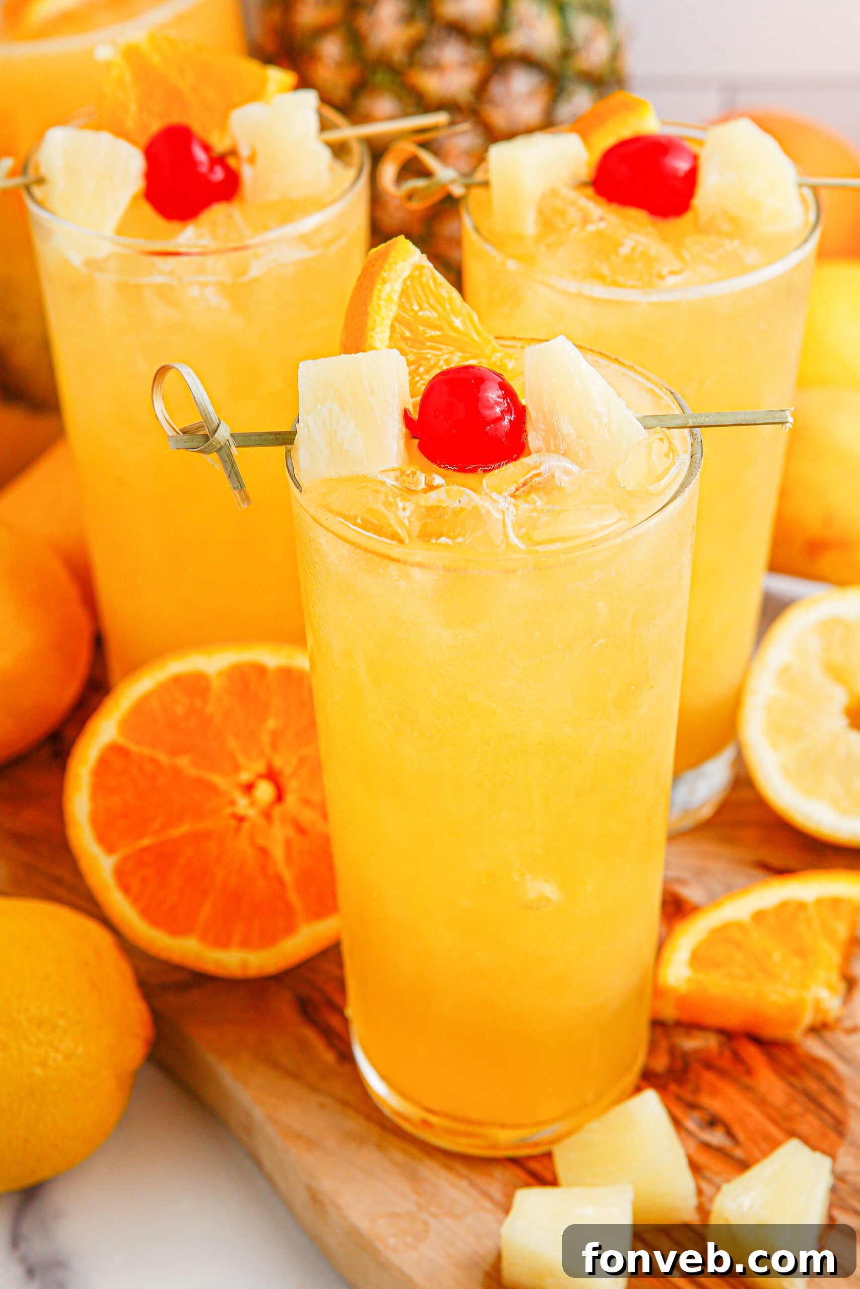 Tropical Lemonade Punch in 3 tall clear glasses on a wooden table with fruit around it and a pineapple in the background 