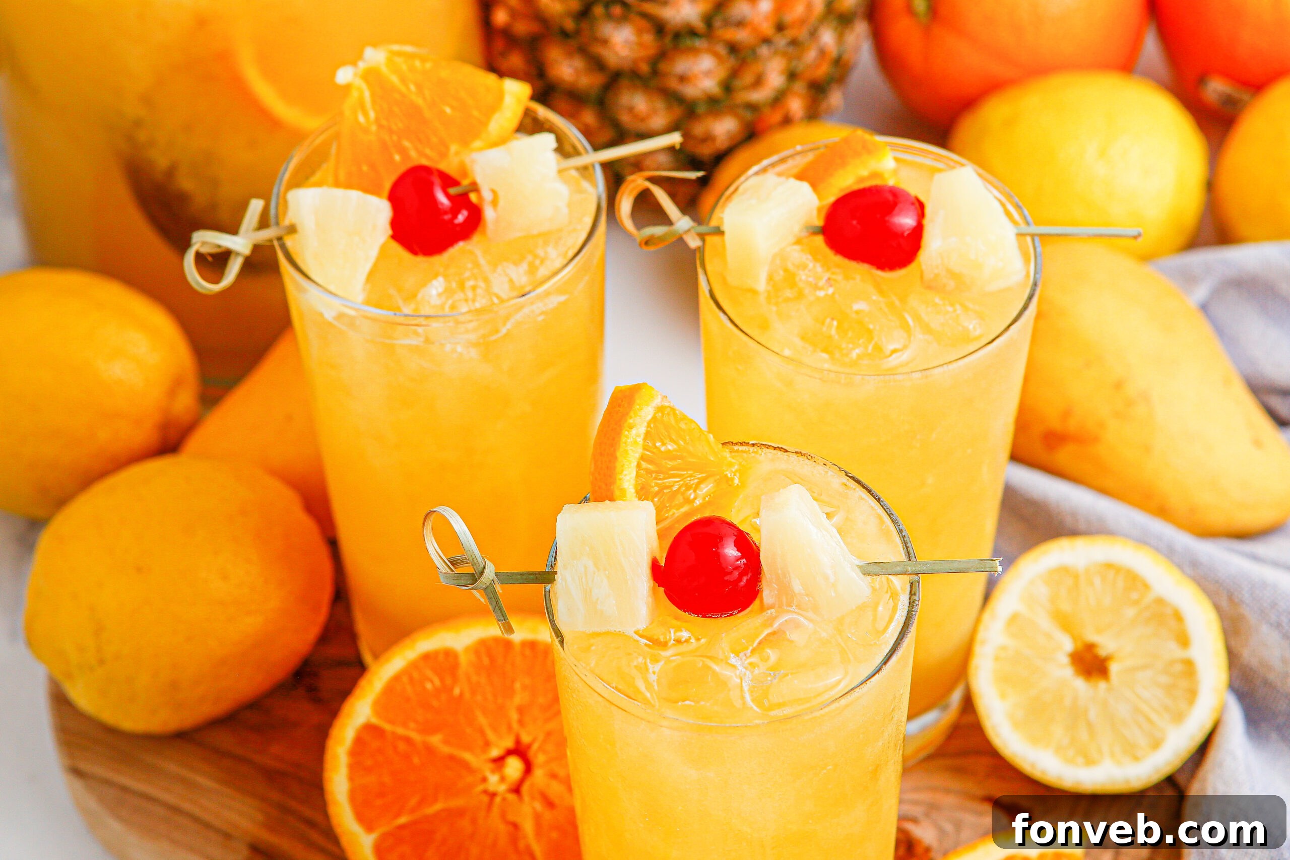 overhead shot of Tropical Lemonade Punch in 3 tall clear glasses on a wooden table with fruit around it