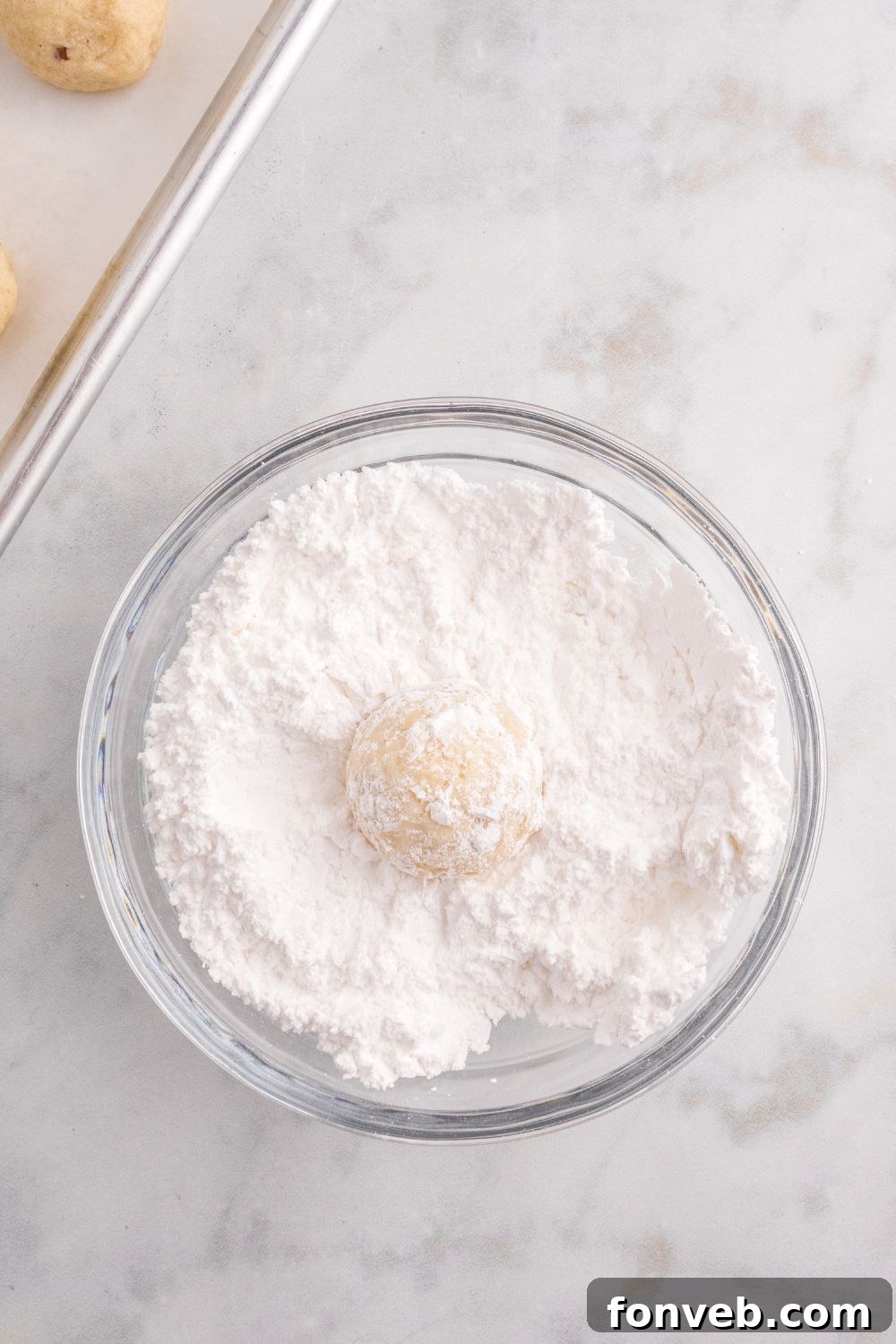 cookie being rolled in a bowl with powdered sugar 