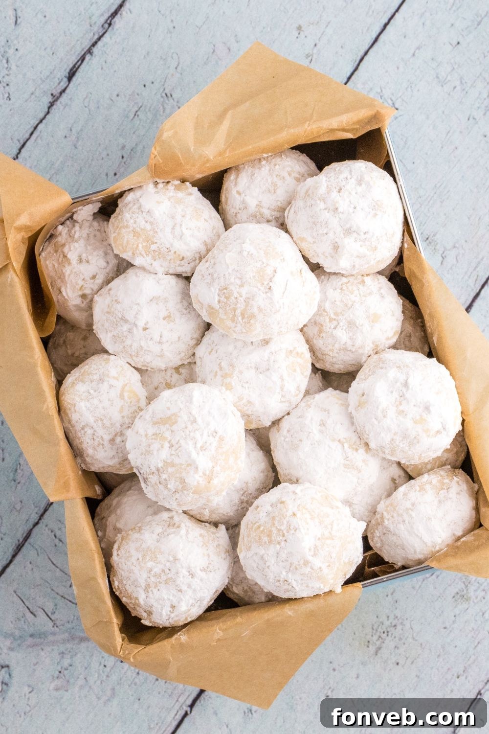 container of snowball cookies sitting on wooden table