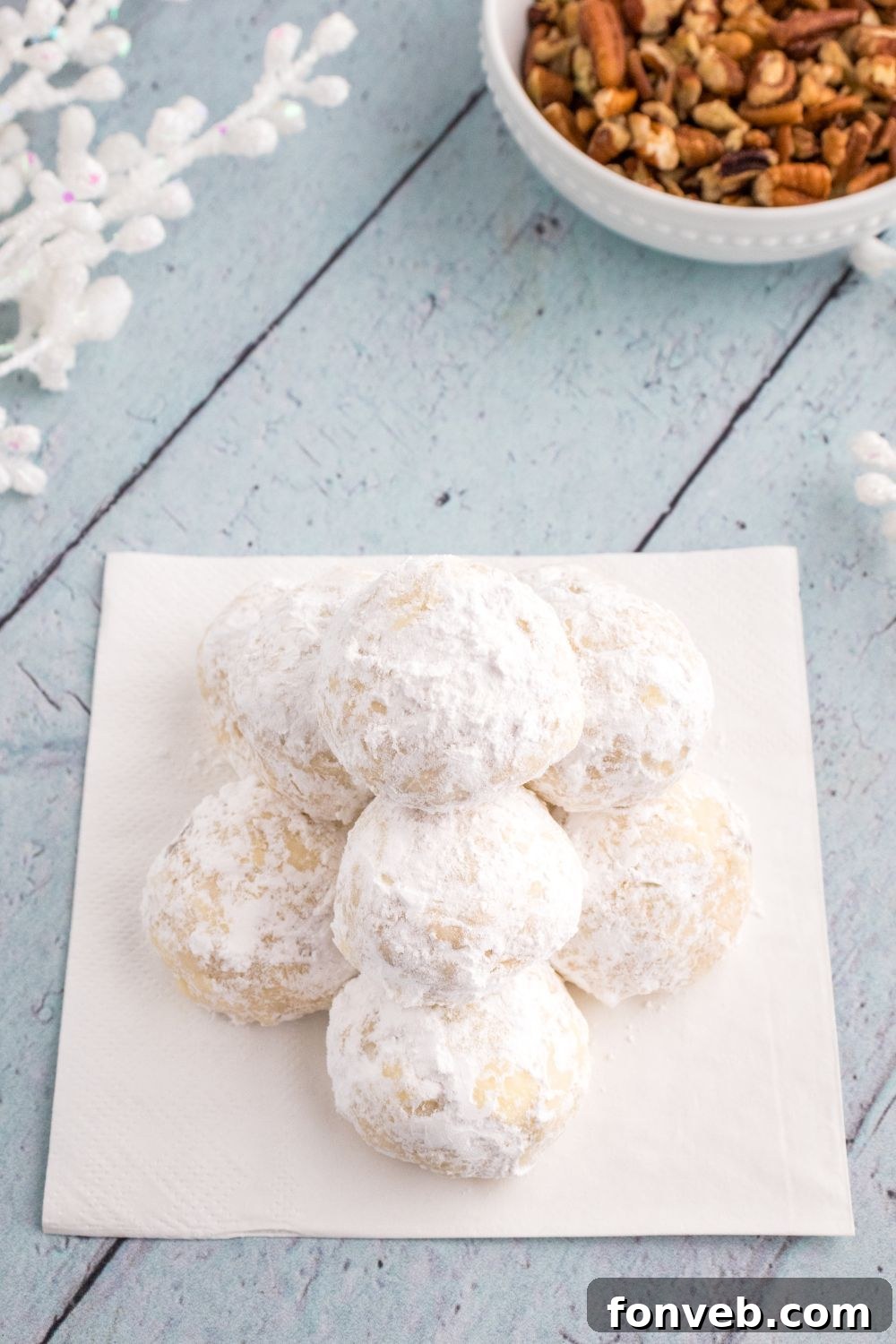 snowball cookies on a plate on table with bowl of nuts behind it